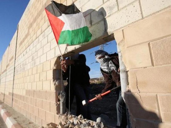 A Palestinian activist knocks a hole through the wall near East Jerusalem