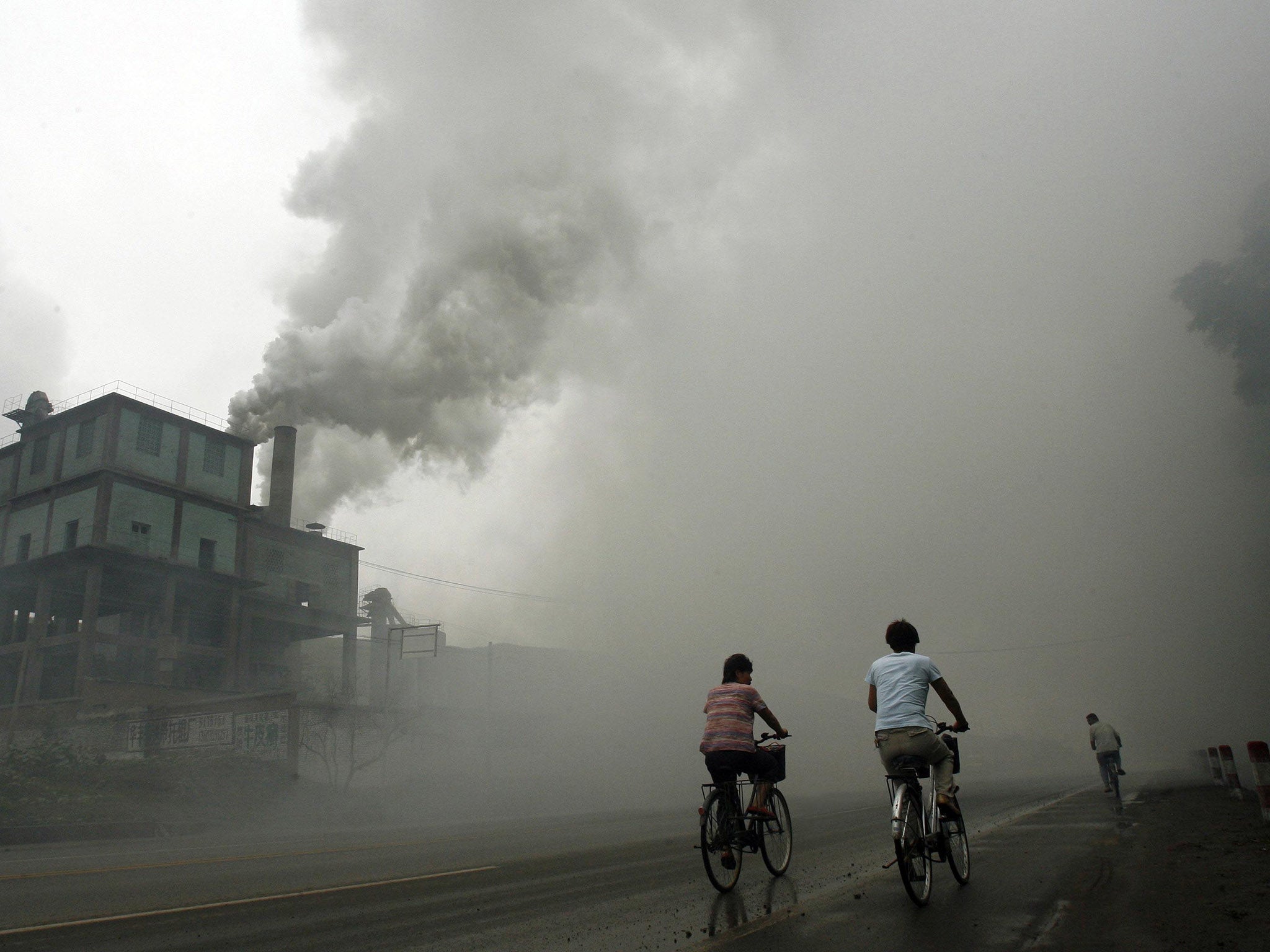 Cyclists pass through thick pollution from a factory in Yutian, 100km east of Beijing in China's northwest Hebei province