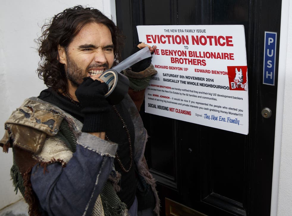 Russell Brand puts a fake eviction notice on The Benyon Estate office as he joins a group of east London residents who protest against rising housing prices 