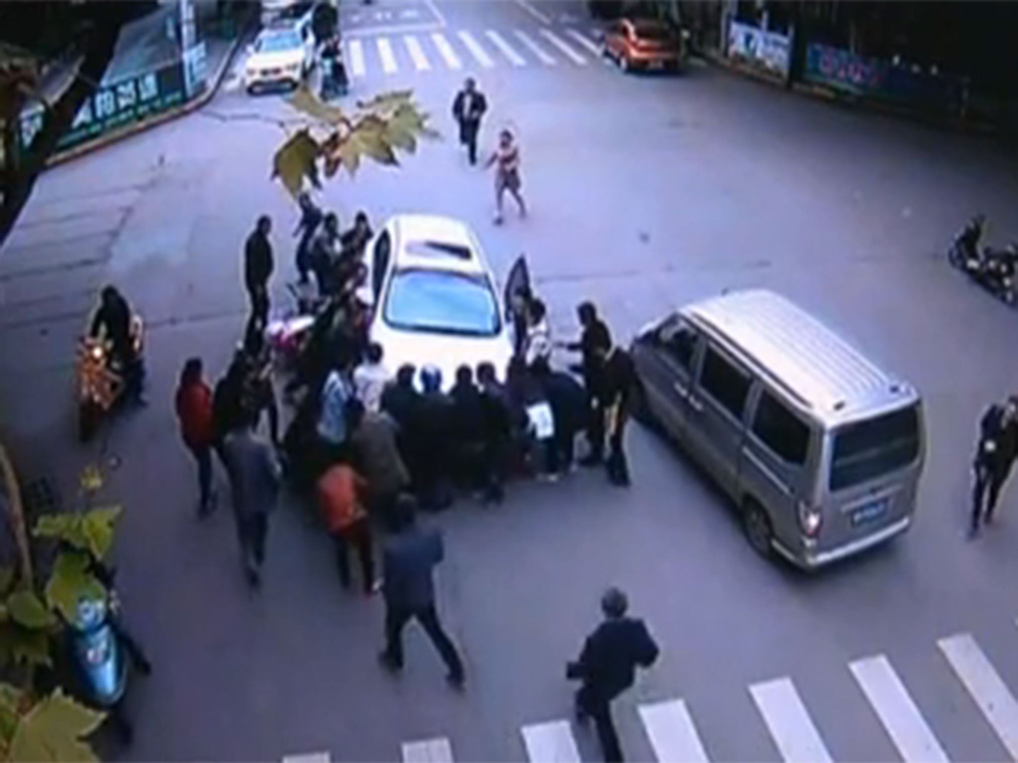 Video from China shows the amazing moment over 20 people rushed to the aid of a woman trapped underneath a car following a crash with the motorbike she was riding on with her husband.