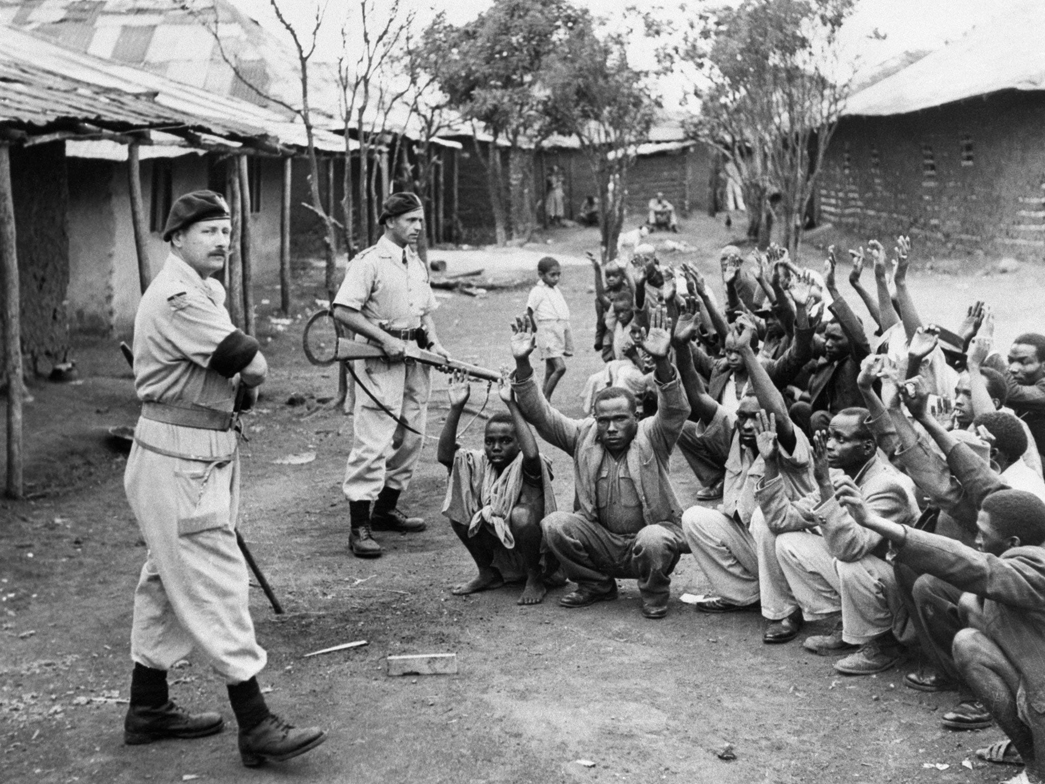 British policemen stand guard over men from the village of Kariobangi, north-east of Nairobi, while their huts are searched for evidence that they participated in the Mau Mau rebellion