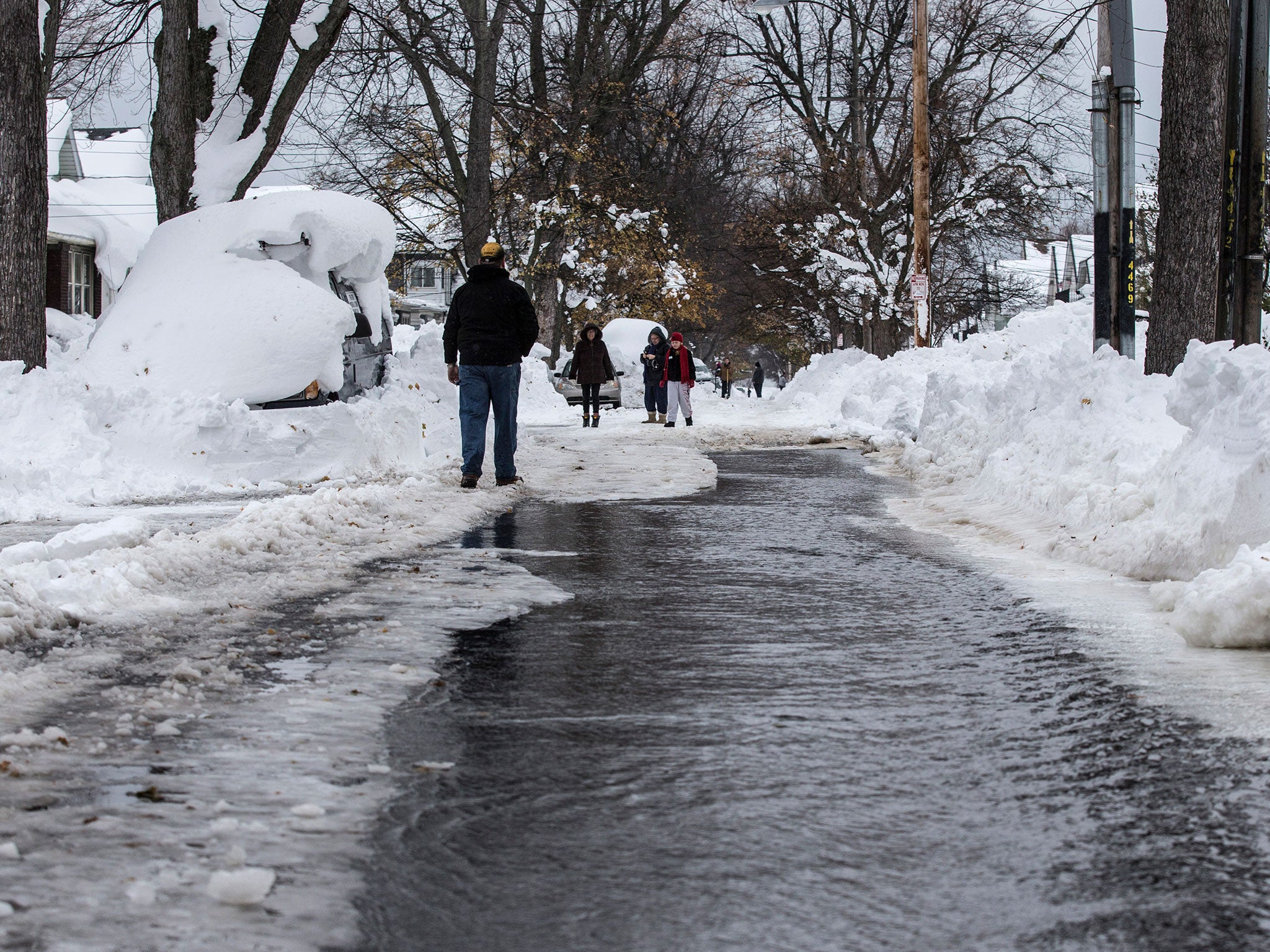 People walk down a street flowing with water after a water main broke in Buffalo, New York November 22, 2014. Warm temperatures and rain were forecast for the weekend in the city of Buffalo and western New York, bringing the threat of widespread flooding