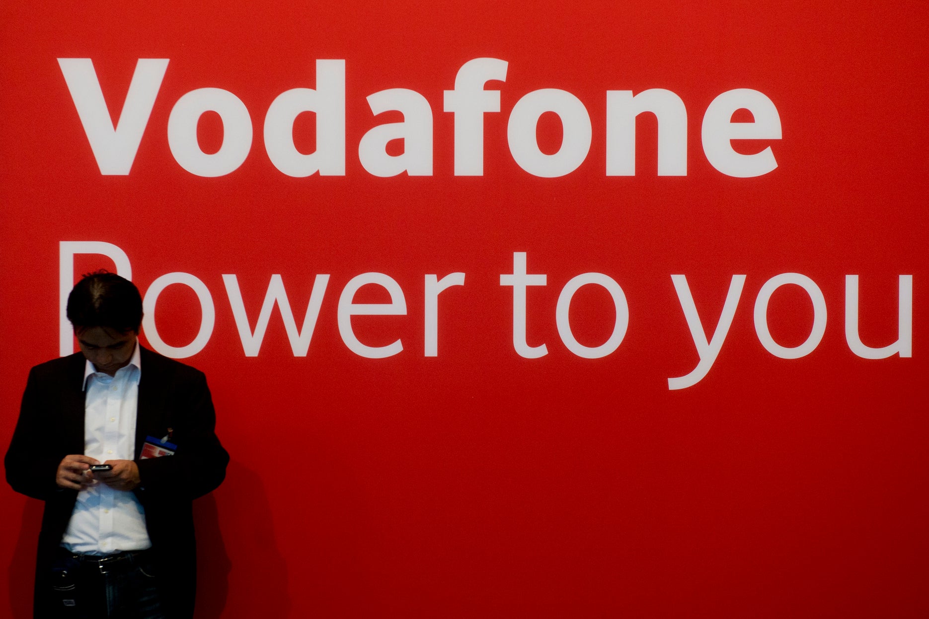 A fair-goer checks his mobile device in front of a Vodafone logo.