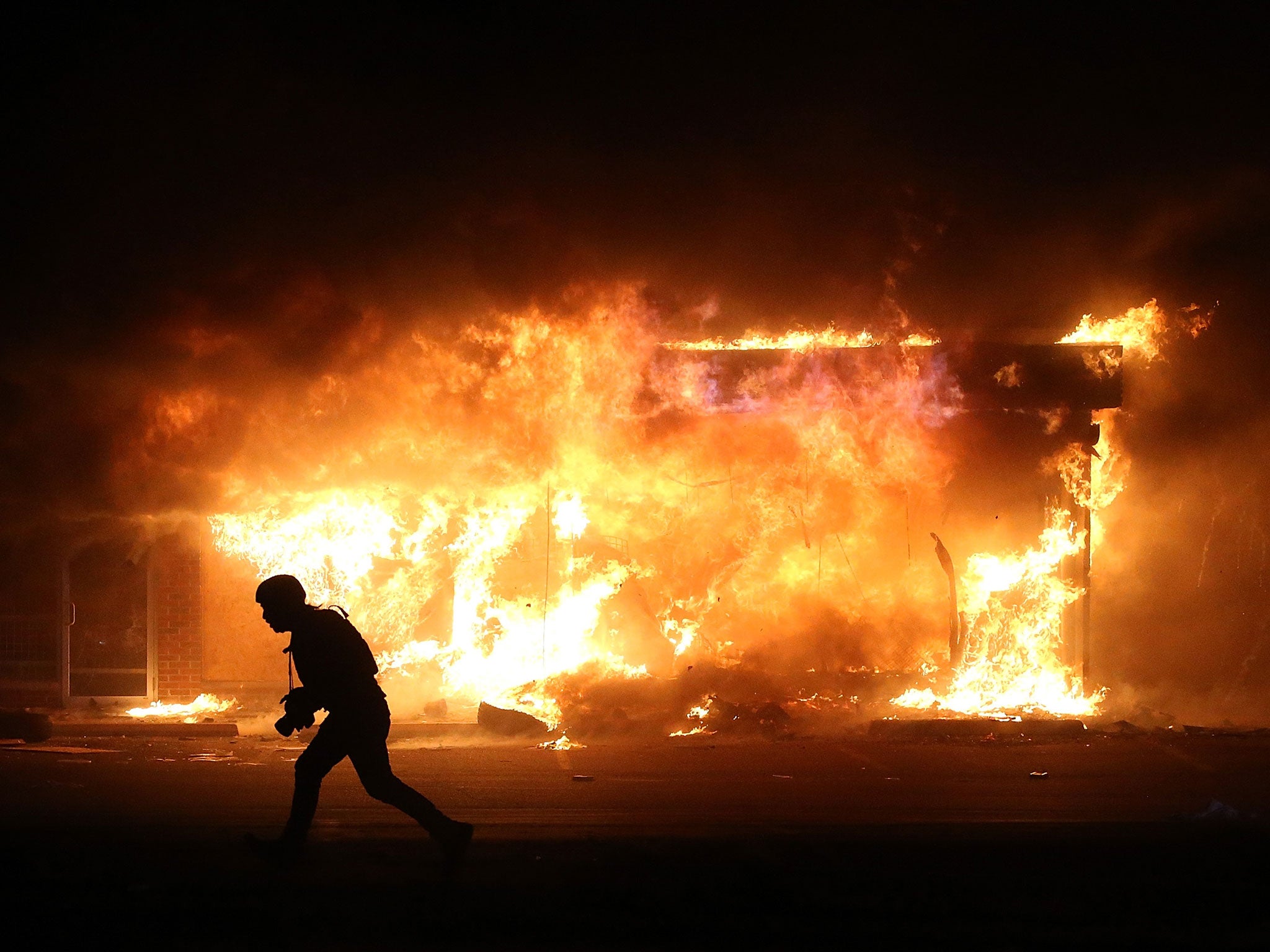 A photographer runs by a burning building during a demonstration on November 25, 2014 in Ferguson, Missouri.