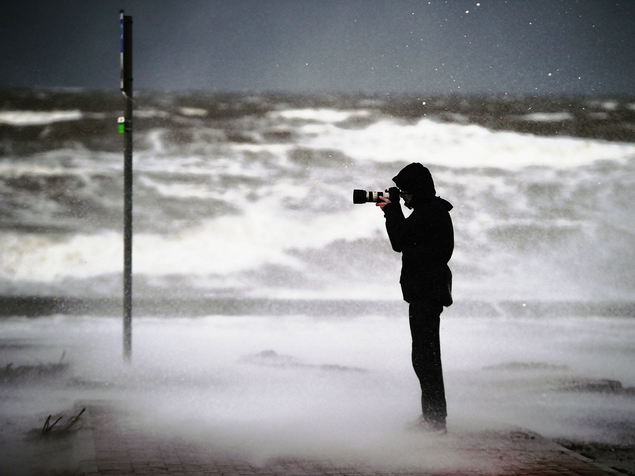 A man takes pictures as waves crash against the promenade wall on 10 December, 2014, in Prestwick, Scotland