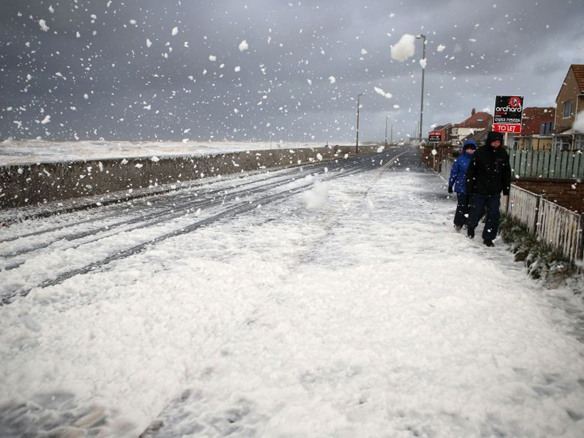 People make their way through foam whipped up by the sea near Blackpool