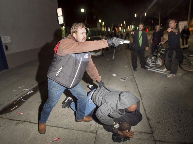 A plain clothes California Highway Patrol detective, who had been marching with anti-police demonstrators, aims his gun at protesters after some in the crowd identified him and his partner during an arrest in Oakland, California