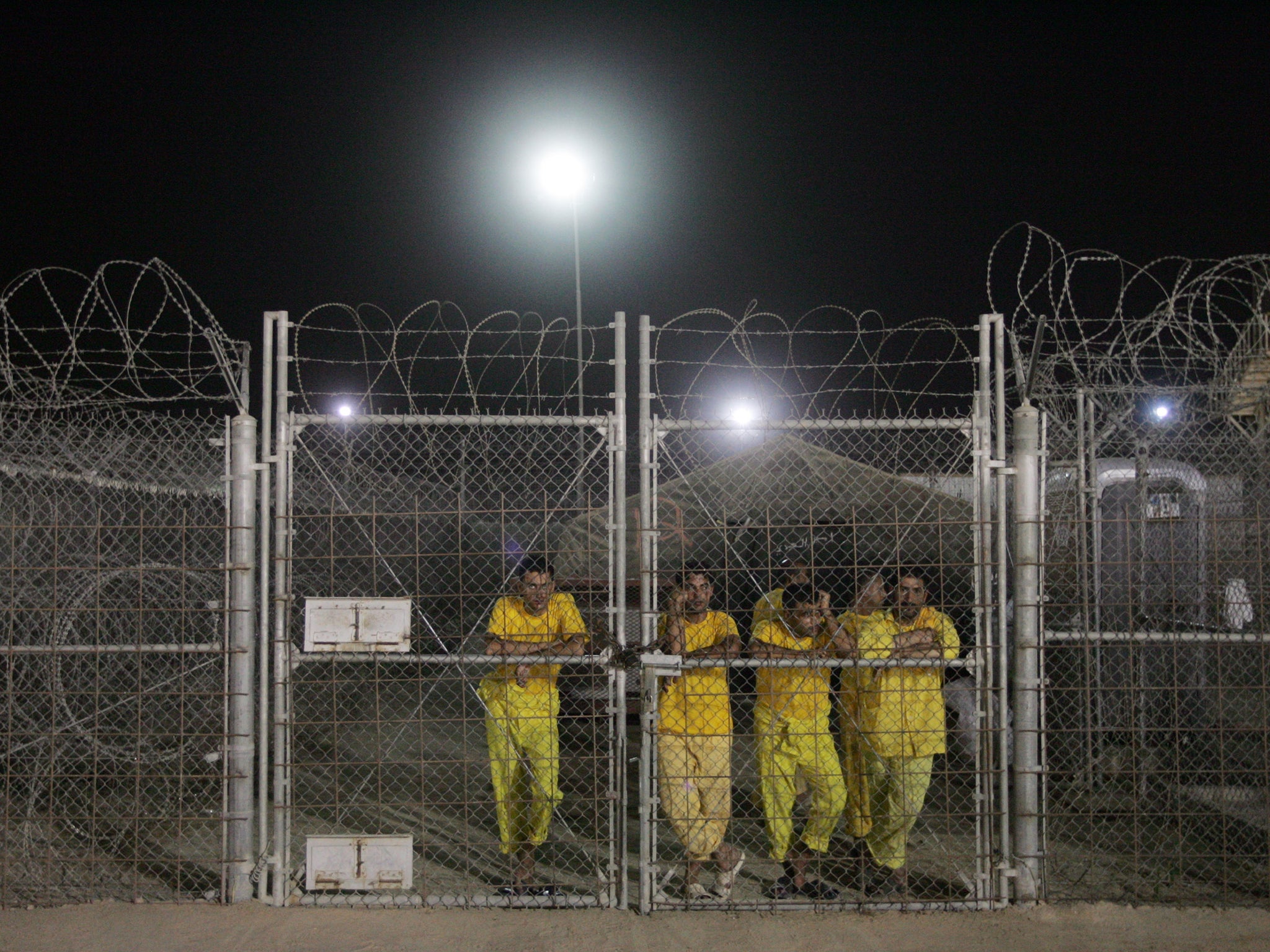 Iraqi detainees stand behind a fence at the Camp Bucca detention centre, located near the Kuwait-Iraq border