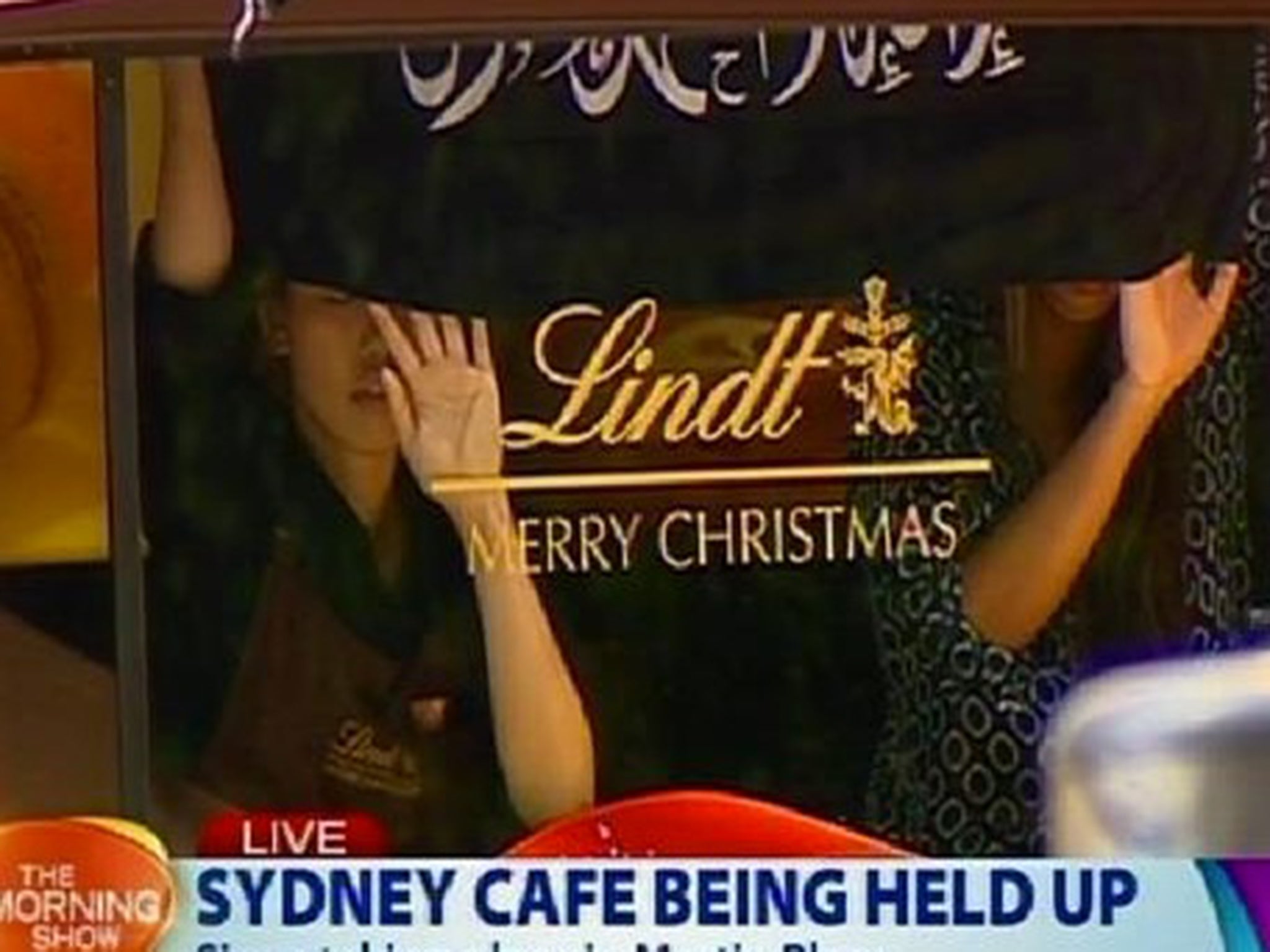 Two hostages hold up a black flag inscribed with Arabic writing during a siege by an Isis-inspired gunman in Sydney