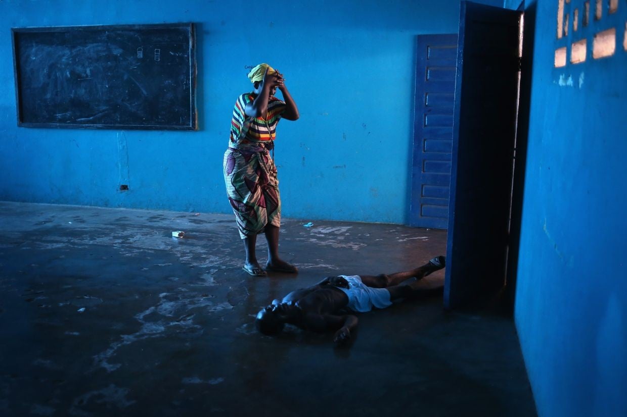 Umu Fambulle stands over her husband Ibrahim after he staggered and fell, knocking him unconscious, in an Ebola ward in Monrovia, Liberia