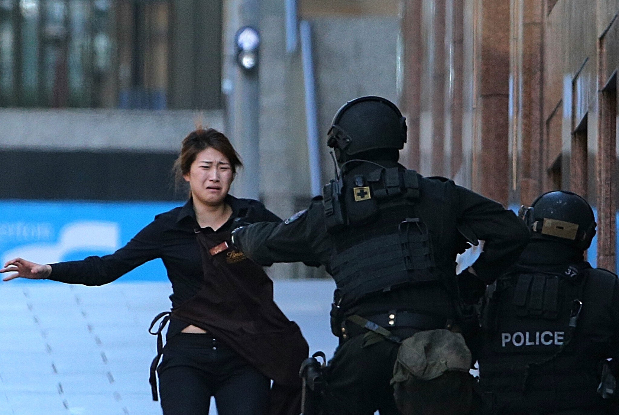 A hostage runs to armed tactical response police officers for safety after she escaped from a cafe under siege at Martin Place in the central business district of Sydney