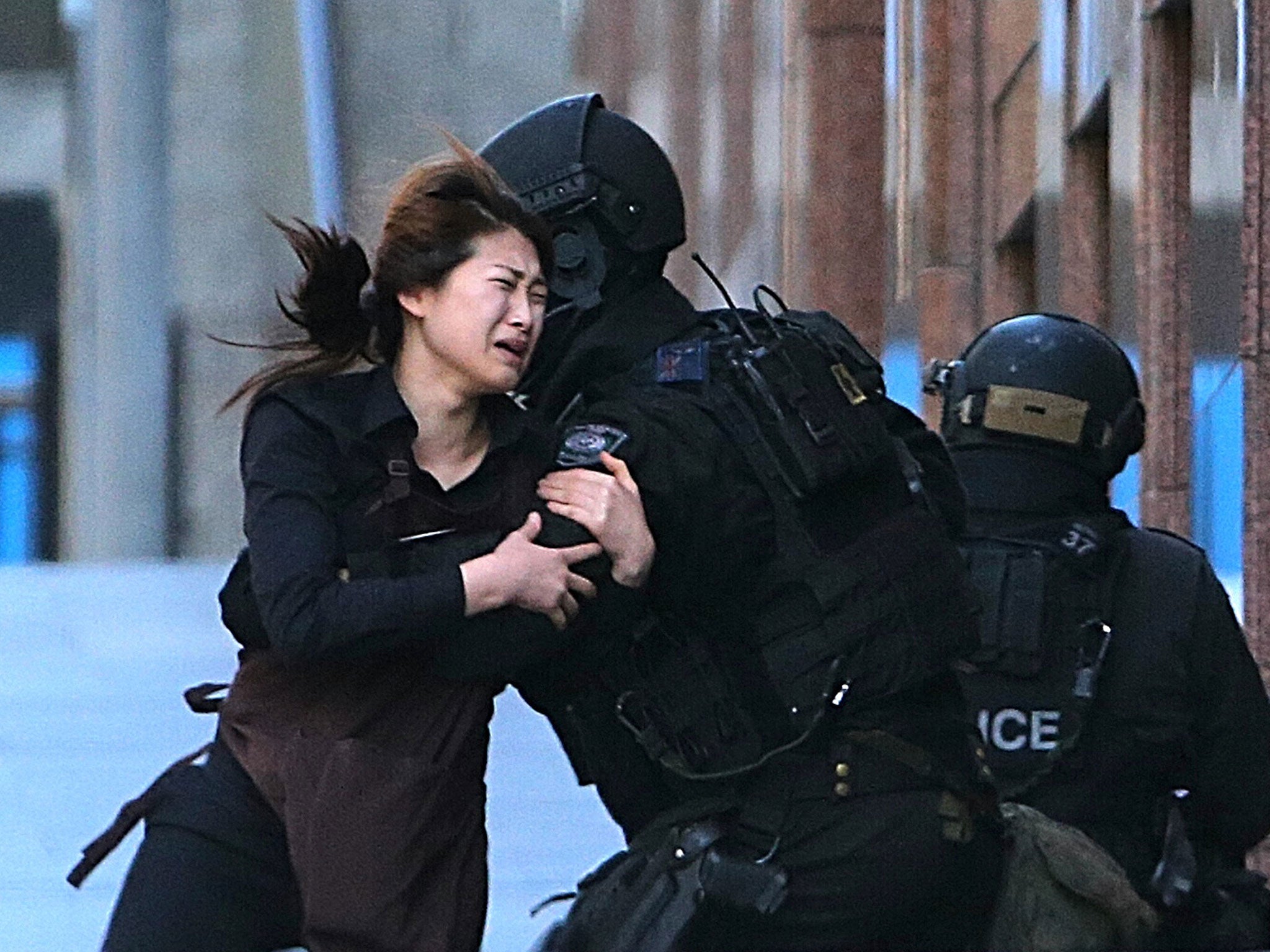 A hostage runs towards a police officer outside a cafe, where other hostages are being held in Sydney