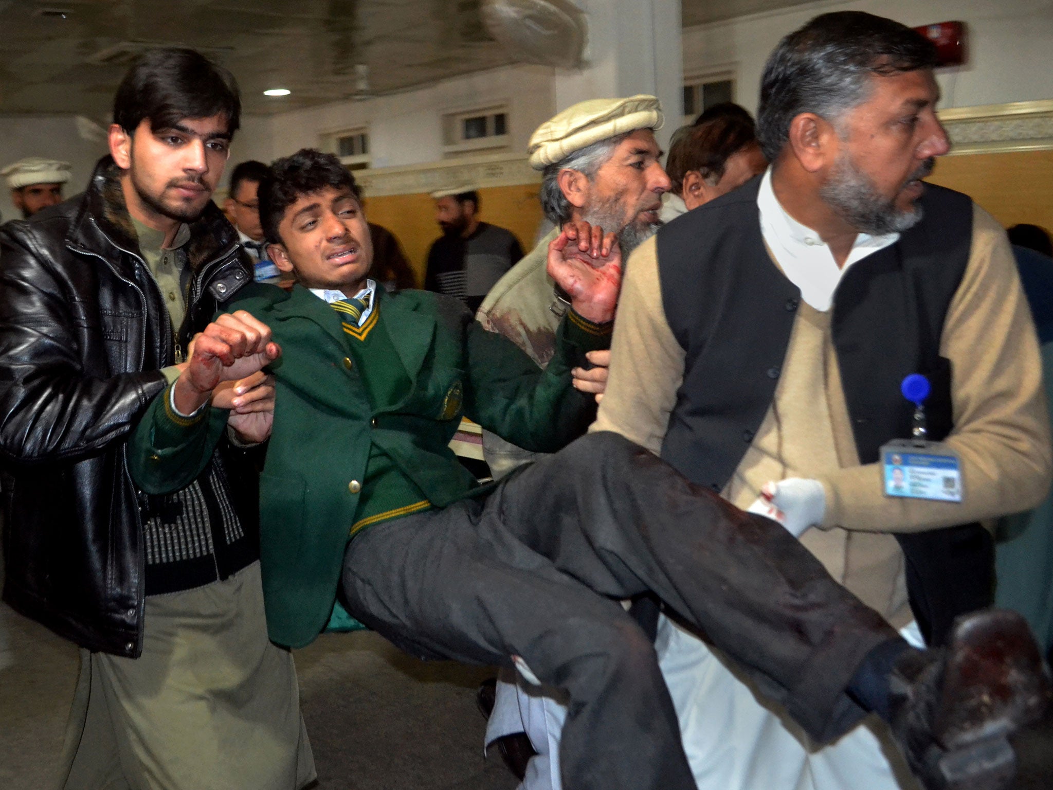Pakistani volunteers carry a student injured in the shootout at a school under attack by Taliban gunmen, at a local hospital in Peshawar