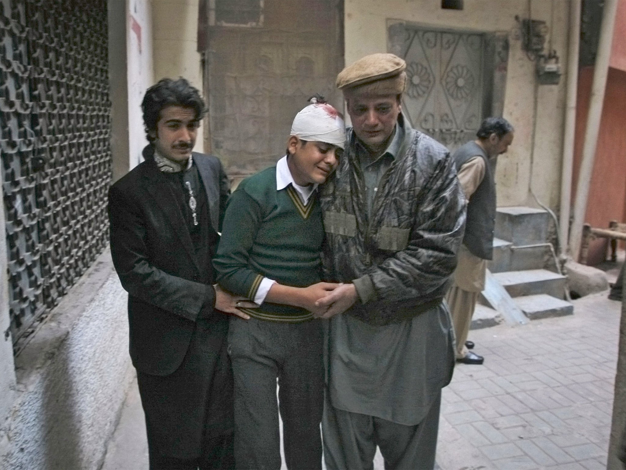 The uncle and cousin of injured student comfort him as he mourns the death of his mother who was a teacher at the school which was attacked by Taliban