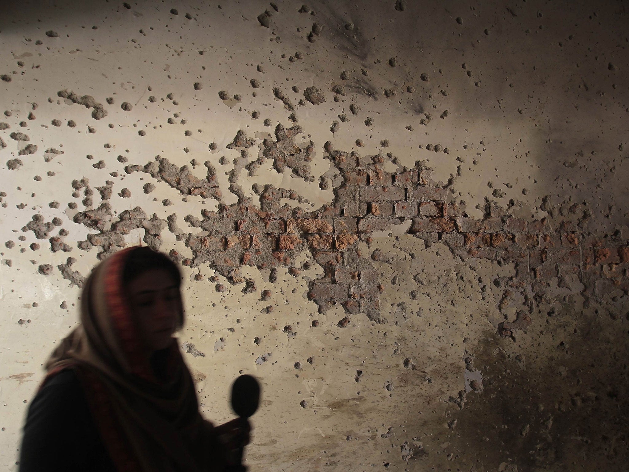 A local reporter walks past a wall full of bullet holes at the Army Public School