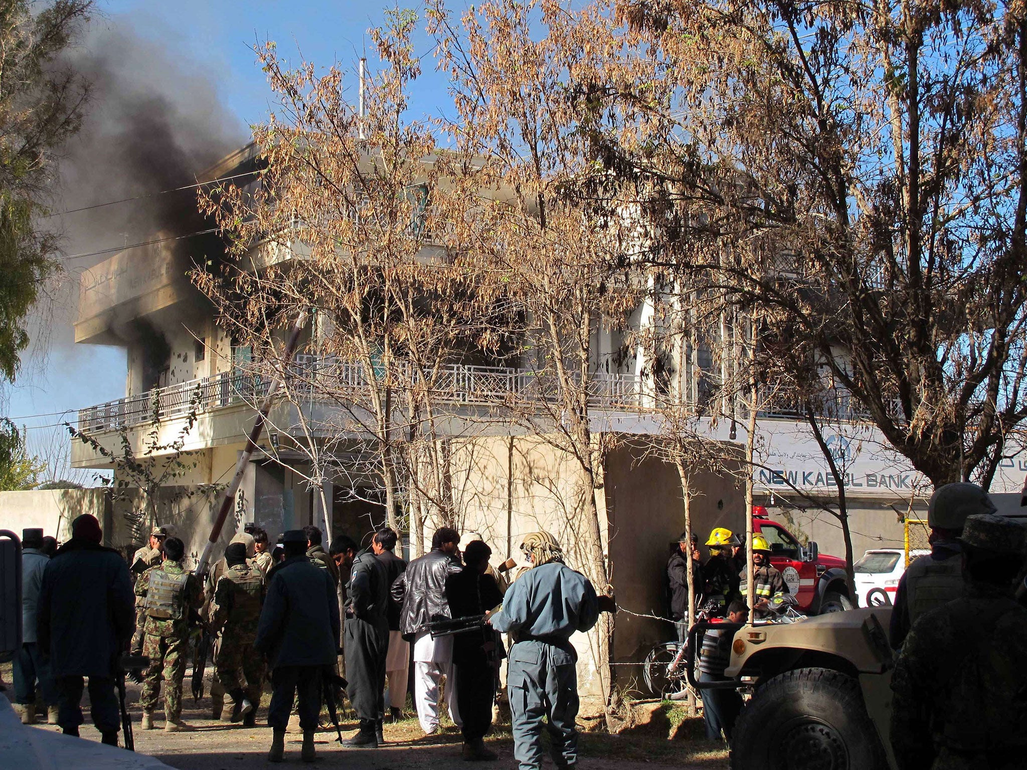 Afghan security forces keep watch as smoke rises from the site of an attack by Taliban suicide bombers at a branch of the Kabul Bank in Lashkar Gah