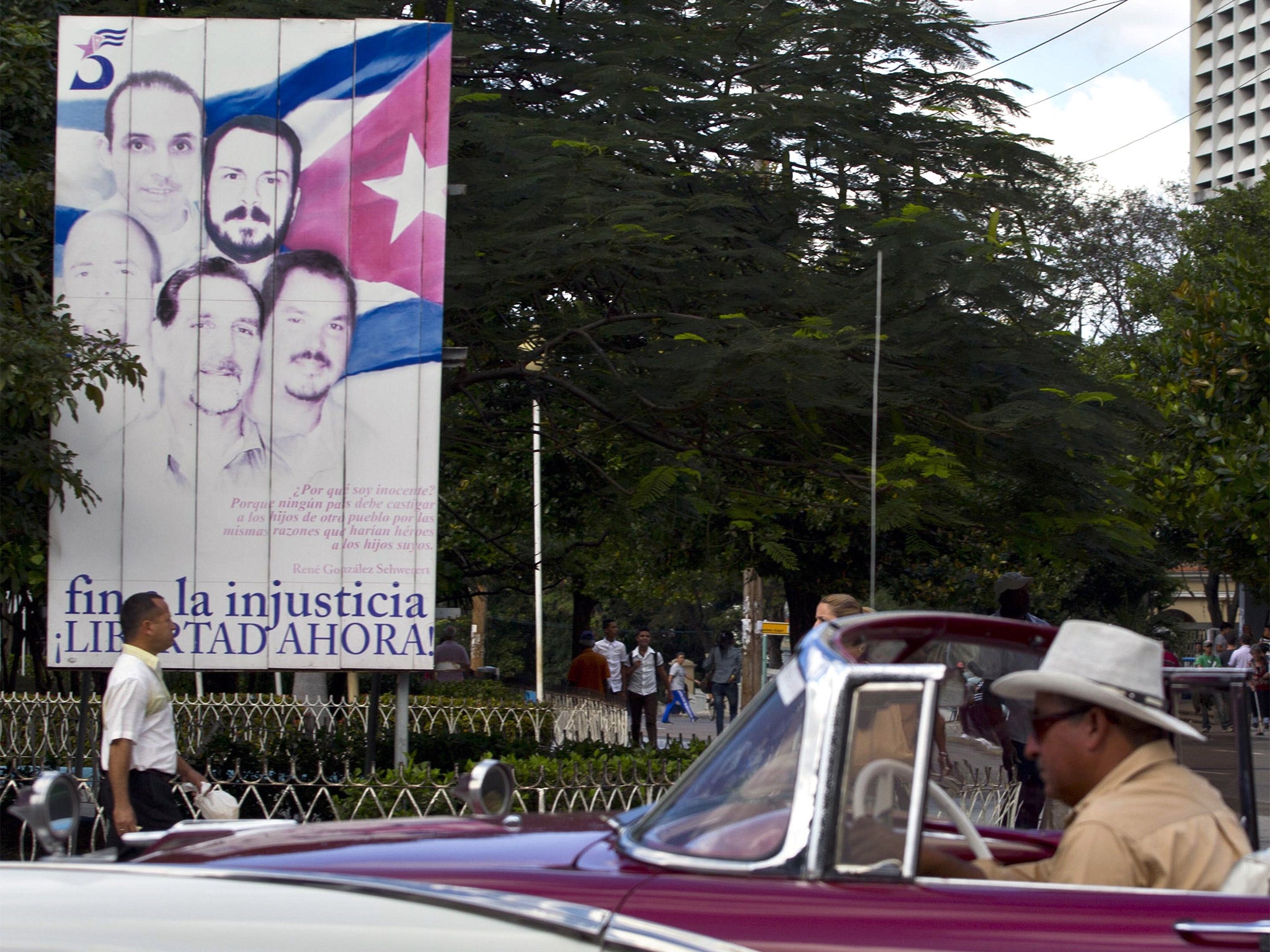 Tourists riding in a classic American car drive by a billboard showing 'The Cuban Five' that reads in Spanish 'End the injustice. Freedom now,' in Havana, Cuba