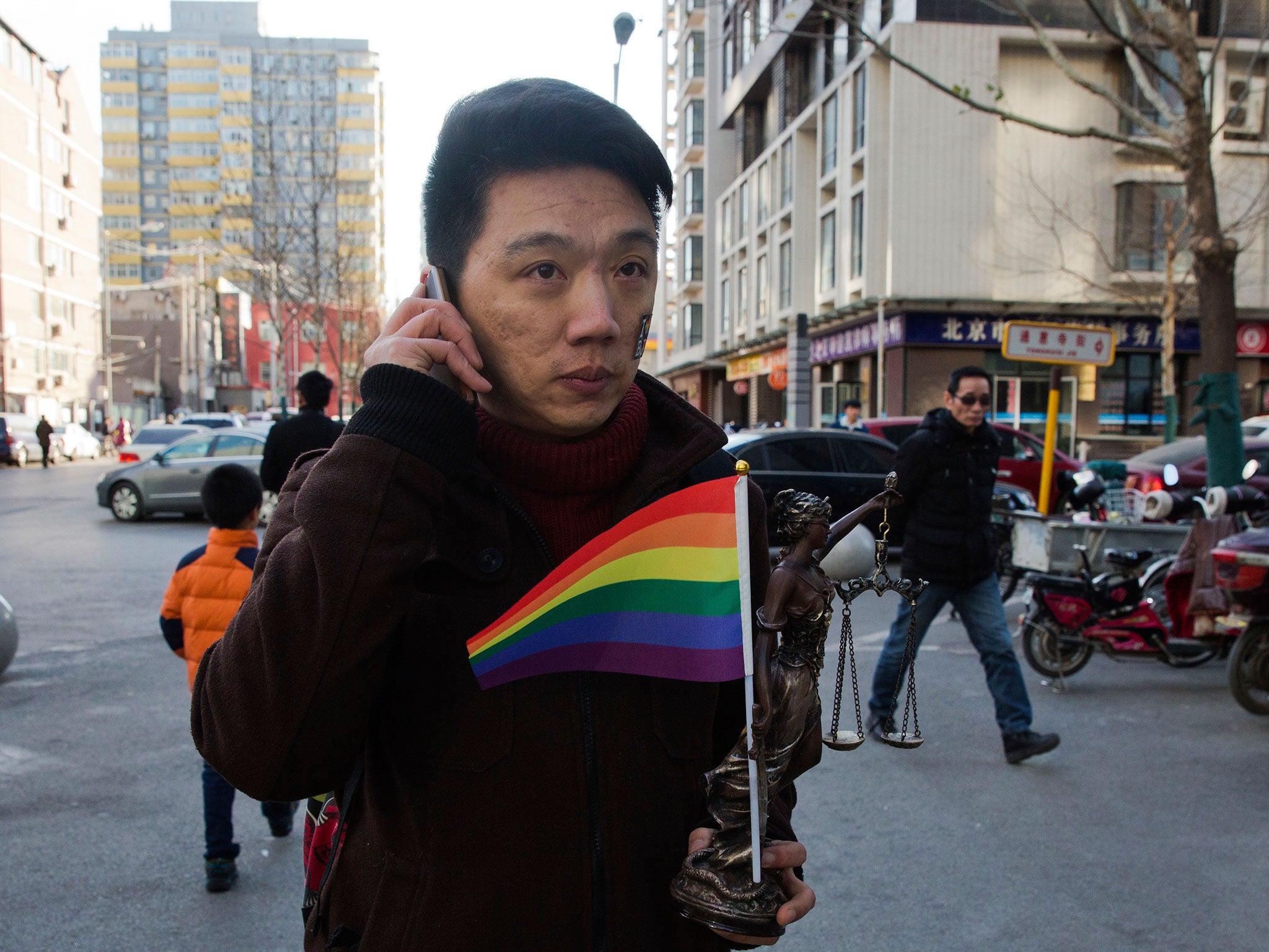 Yang Teng holds up a statue depicting a goddess of justice and a rainbow color flag as he arrives to attend a court verdict in Beijing, China, Friday, Dec. 19, 2014