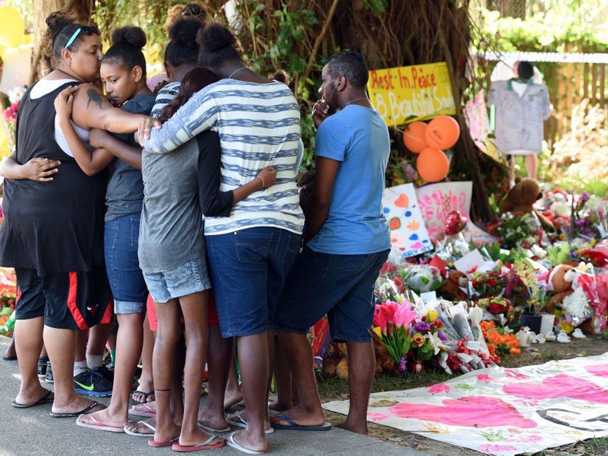 Mourners comfort each other while attending a floral tribute near the house