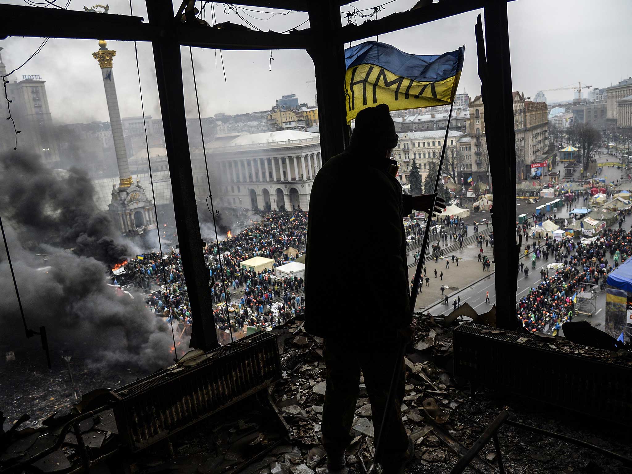 A protester holds an Ukranian national flag from a burned building during a face-off against police in Kiev in February