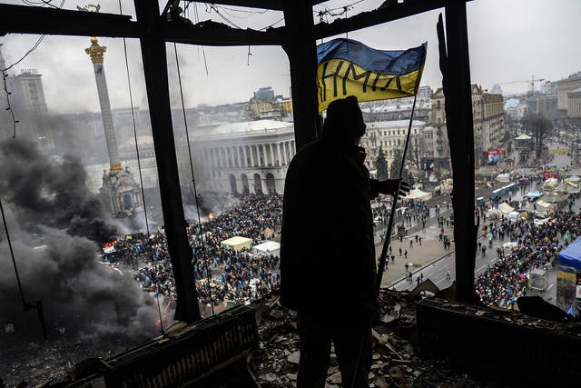 A protester holds an Ukranian national flag from a burned building during a face-off against police in Kiev in February