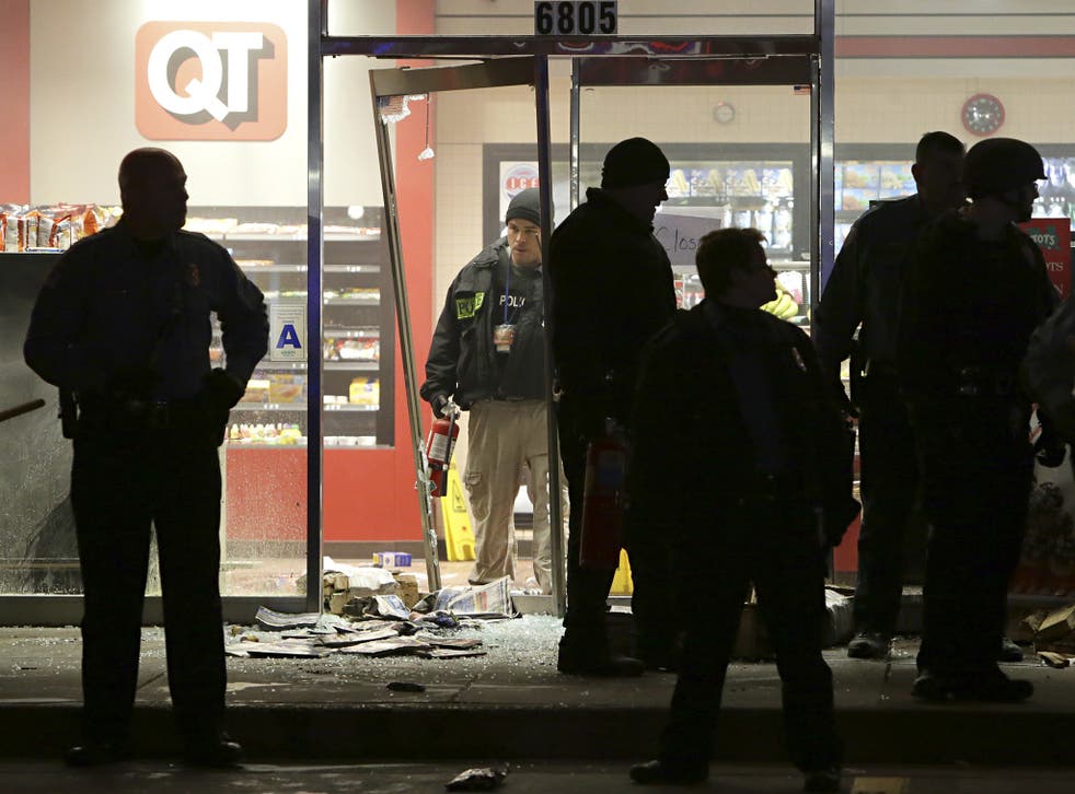 A police officer with a fire extinguisher stands in the broken out entry to a QuikTrip convenience store following the shooting