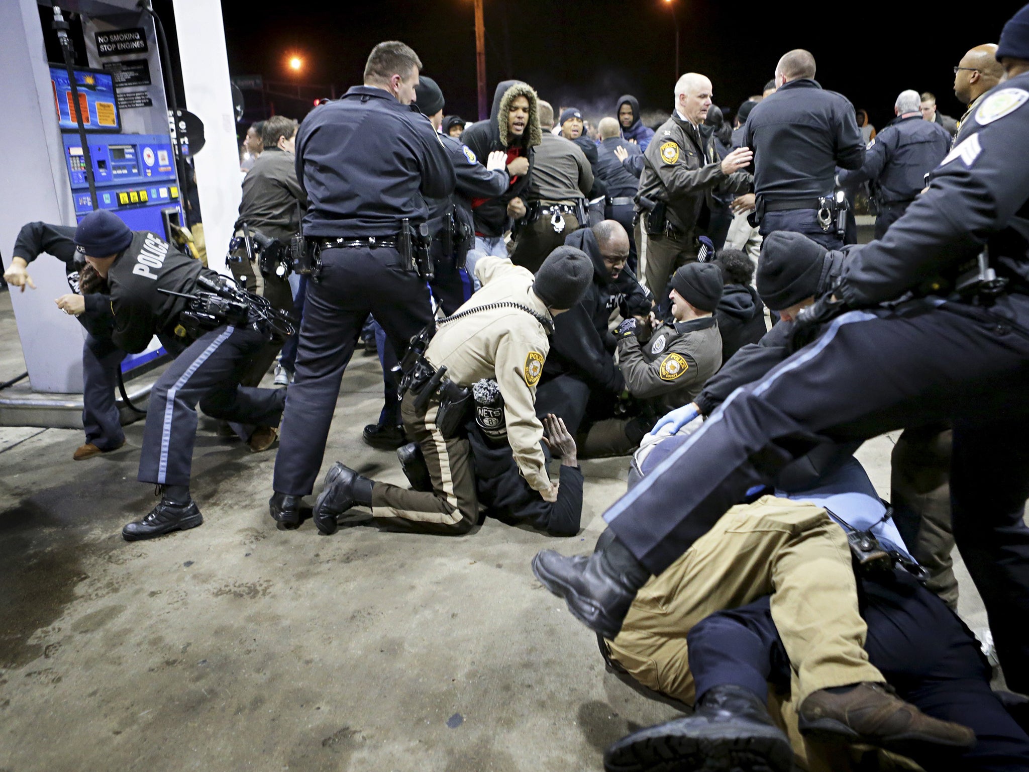 Police try to control a crowd on the lot of a gas station