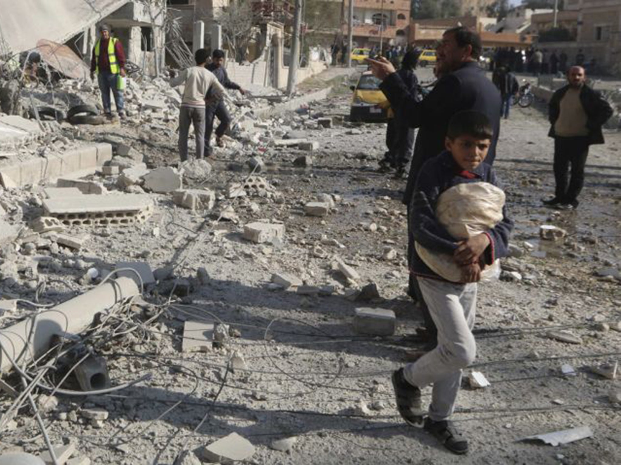 A boy carries bread as he walks past buildings in Raqqa destroyed by an air strike. Residents say water and electricity supplies are intermittent and food is running short