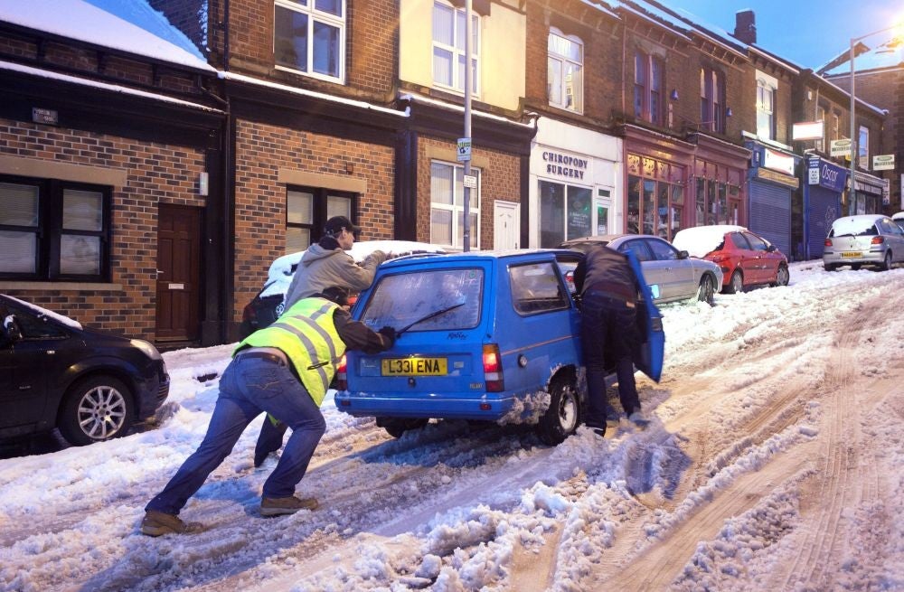 People push a car in snowy conditions in the Crookes area of Sheffield after wild and wintry weather swept the UK