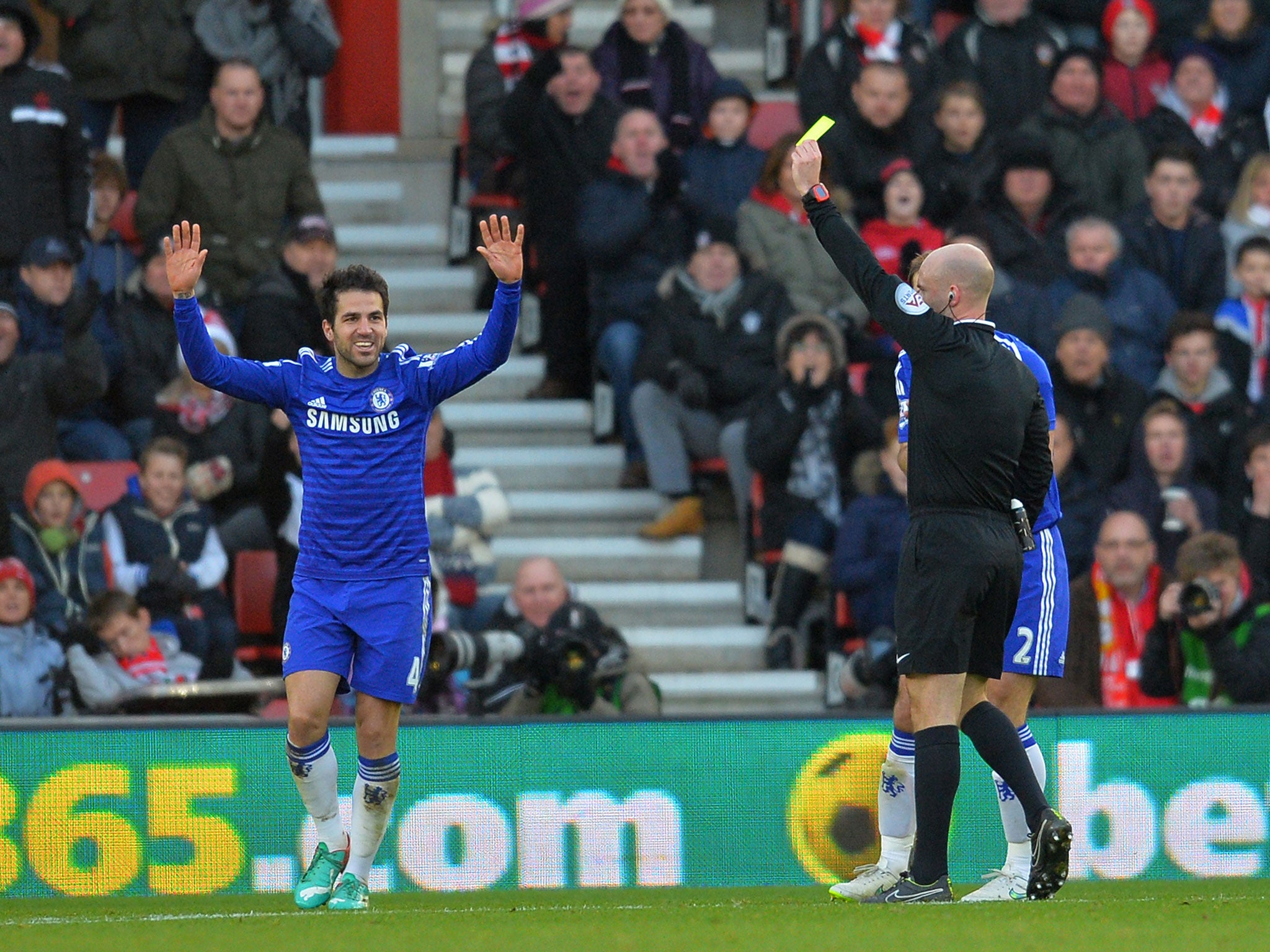 Cesc Fabregas receives his yellow card from Anthony Taylor