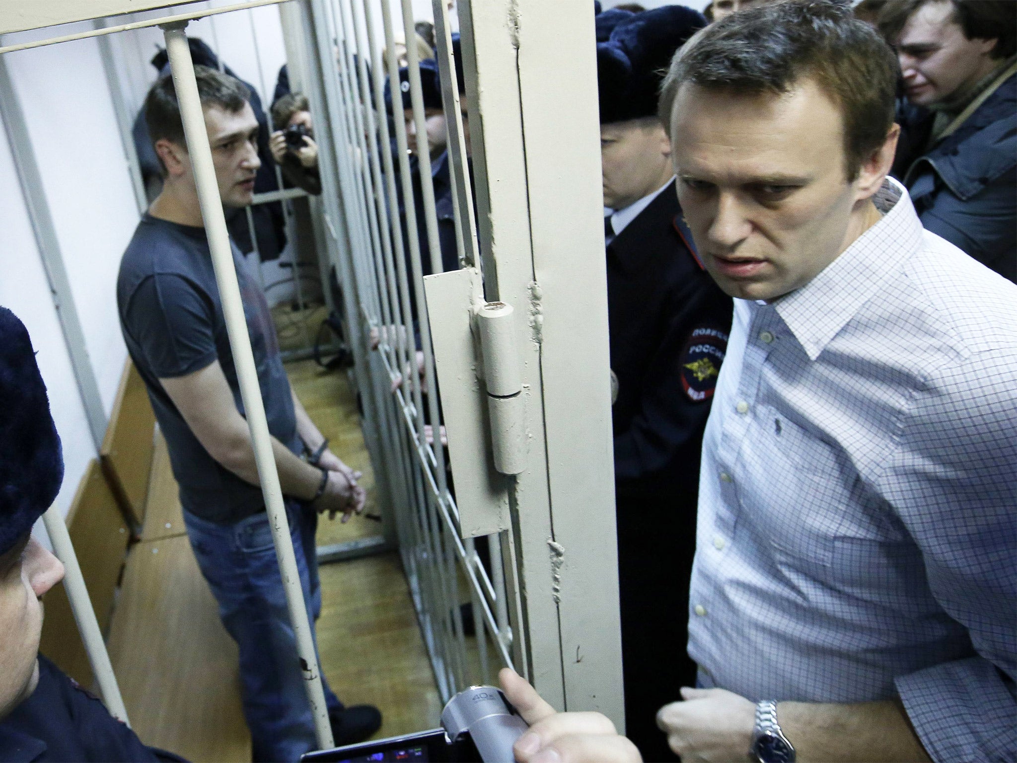 Alexei Navalny (right) and his brother and co-defendant Oleg (inside the cage) at a court hearing in Moscow yesterday; Oleg received a custodial sentence, Alexei a suspended sentence