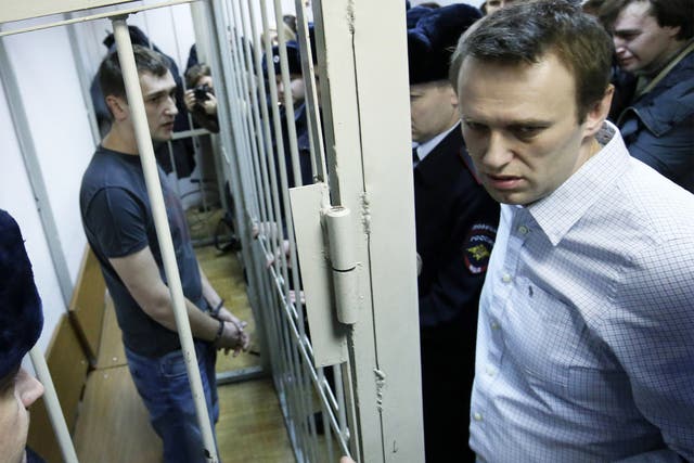 Alexei Navalny (right) and his brother and co-defendant Oleg (inside the cage) at a court hearing in Moscow yesterday; Oleg received a custodial sentence, Alexei a suspended sentence