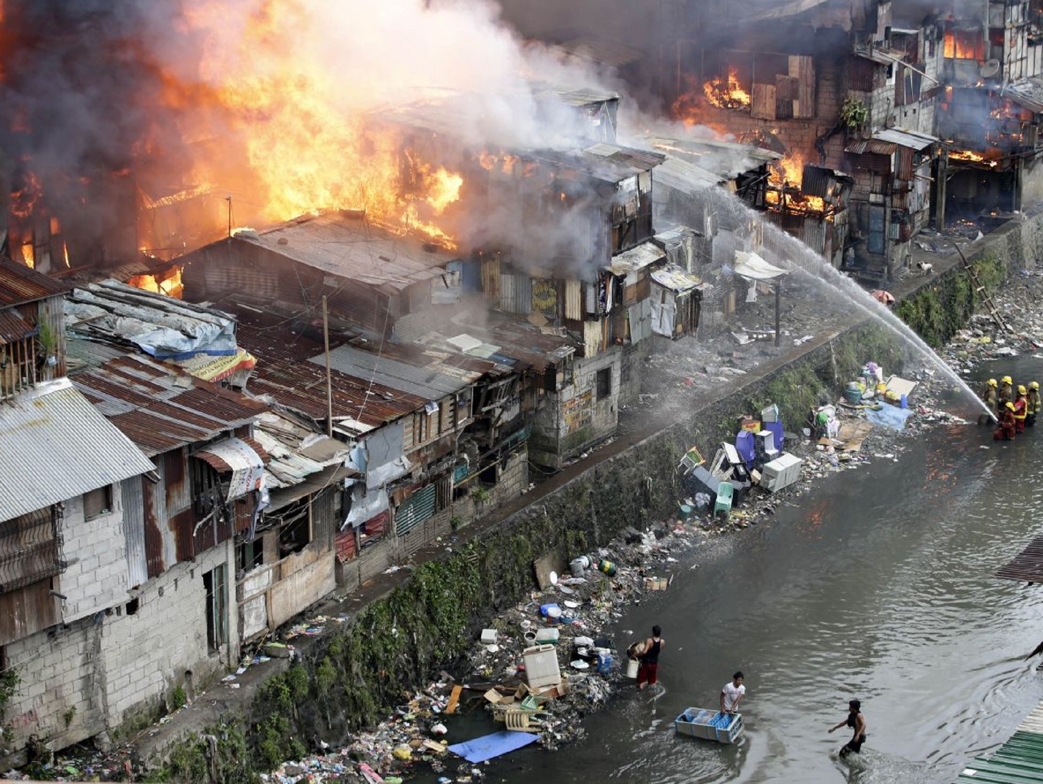 Firefighters battle the flames with hoses while standing in the creek in the Philippines