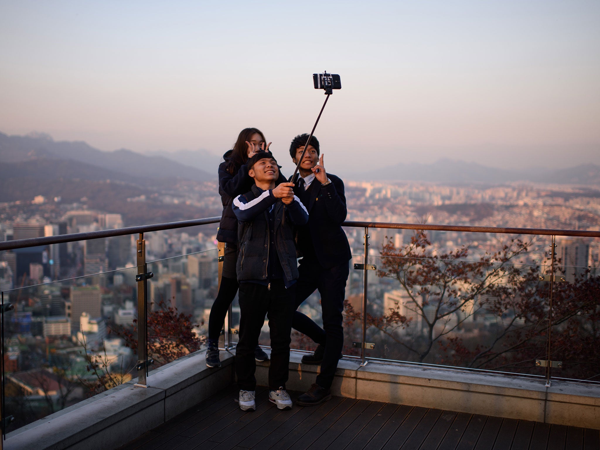 People use a 'selfie stick' to take a group photo overlooking the city skyline of Seoul
