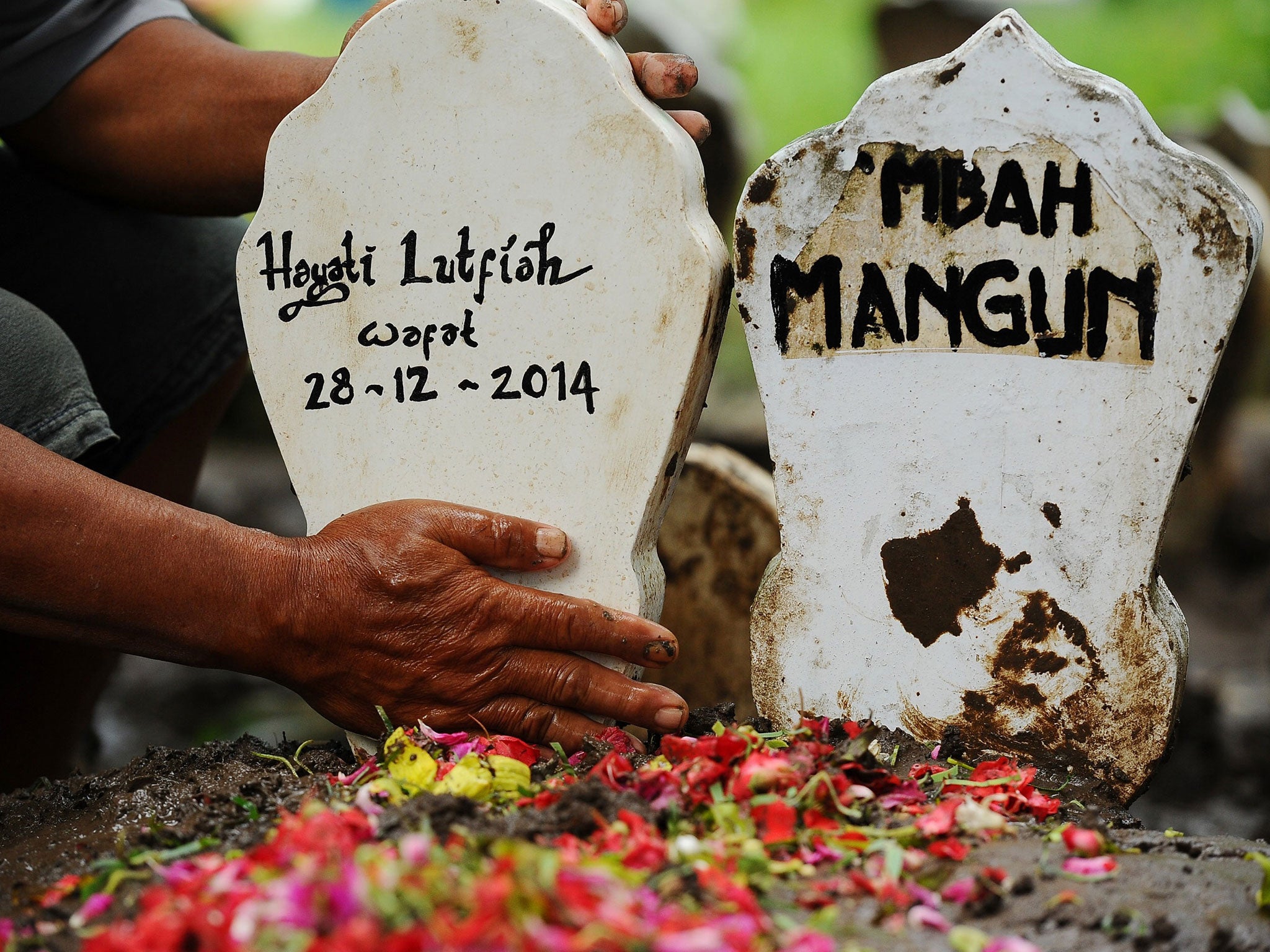 Subekti, a tomb caretaker cleans up Hayati Lutfiah Hamid's grave, the first identified victim of the AirAsia flight QZ8501 crash at Sawo Tratap Islamic cemetery in Surabaya, Indonesia