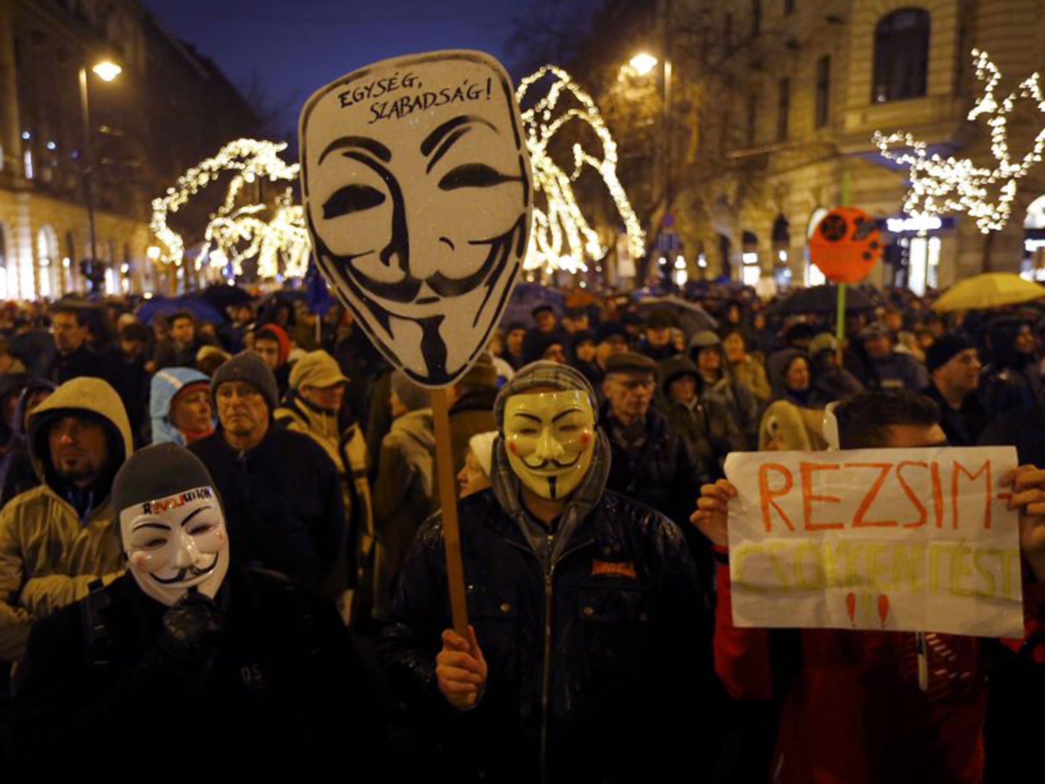 Anti-government protesters wear Guy Fawkes masks and hold a placard reading ‘regime’ in Budapest last week (Reuters)