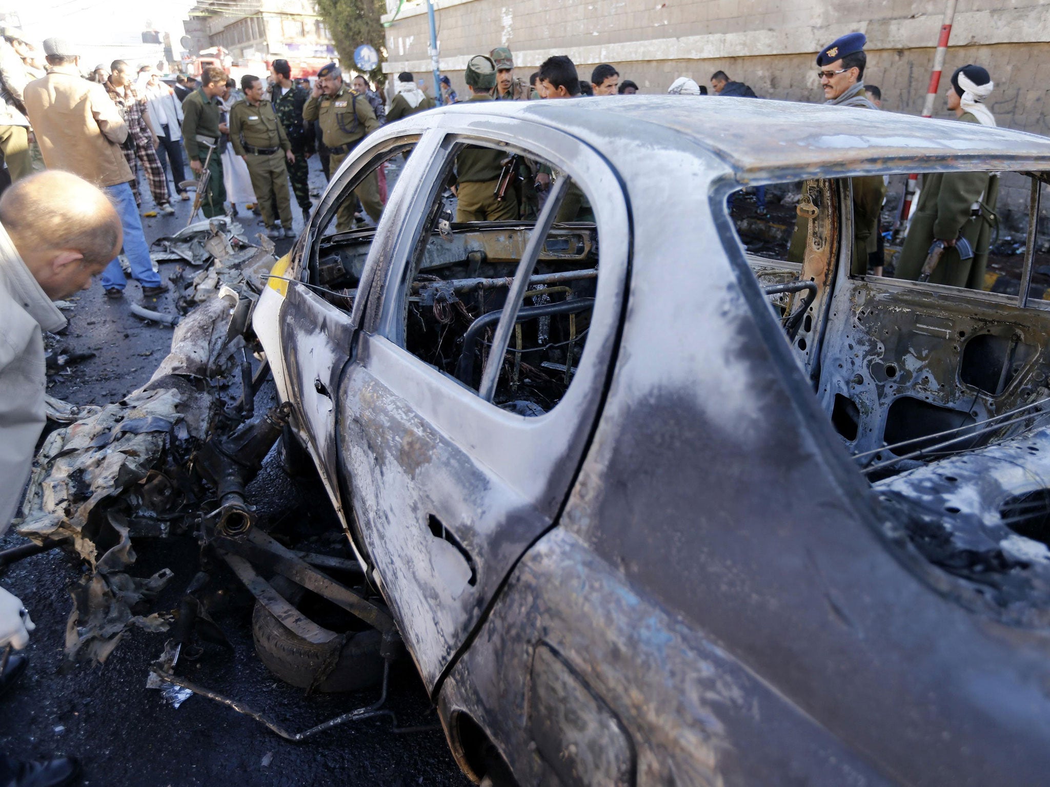 A police investigator looks at a damaged car at the scene of a car bomb outside the police college in Sanaa