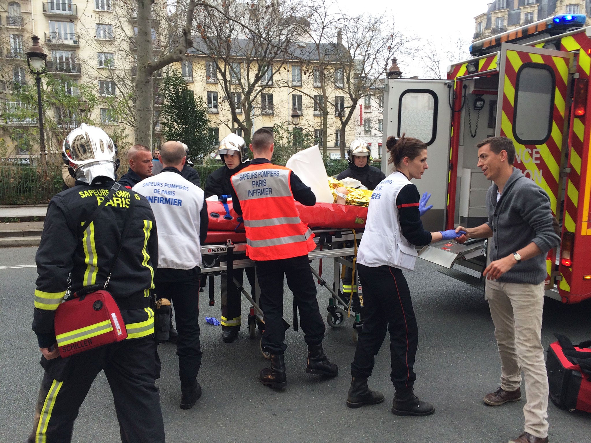 Firefighters carry an injured man on a stretcher in front of the offices of the French satirical newspaper Charlie Hebdo in Paris