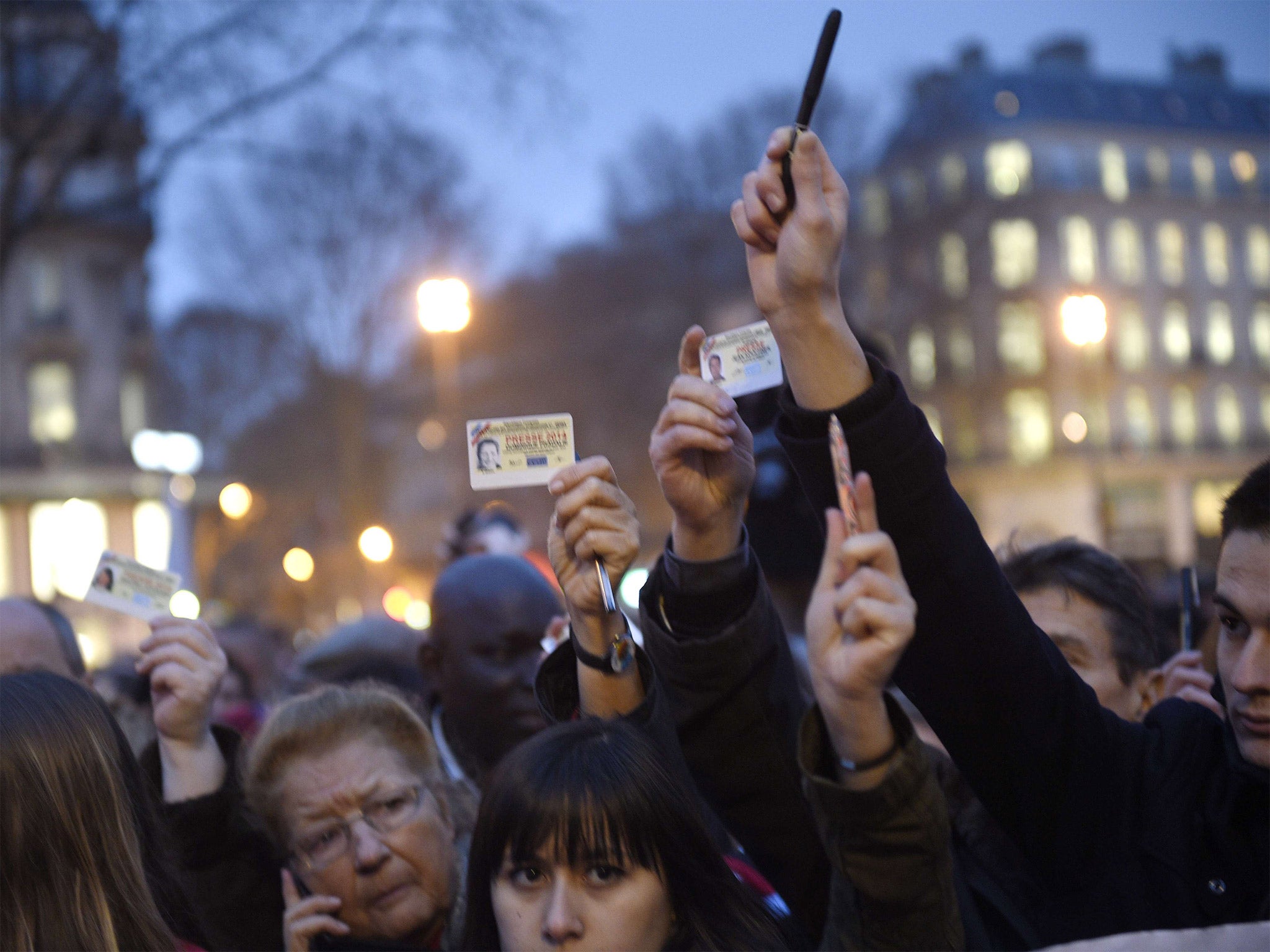 Journalists raise their press cards as others hold up pens during a gathering at the Place de la Republique, following the terrorist attack on the offices of the satirical weekly, 'Charlie Hebdo'