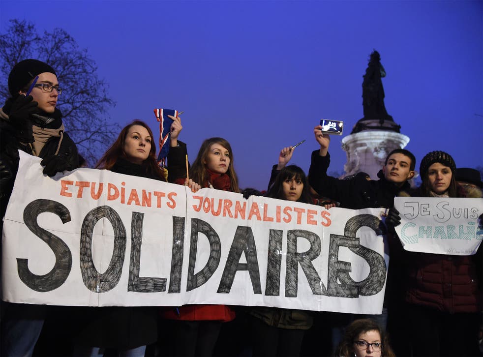 Journalism students hold a banner reading in French: 'Journalism students : Solidarity' as they raise pens during a gathering at the Place de la Republique in Paris