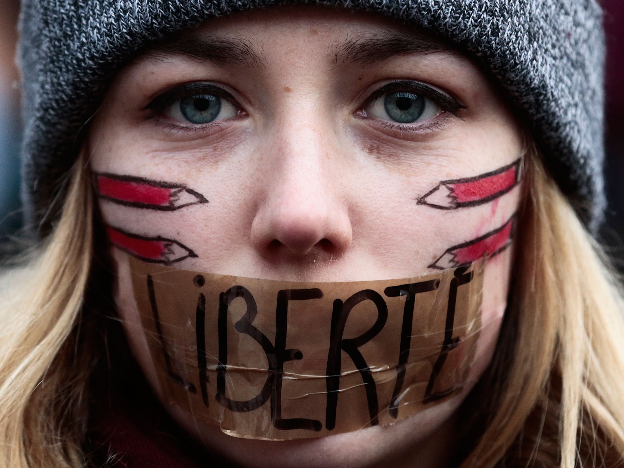 A woman has taped her mouth with the word Freedom as she gathers with several thousand people in solidarity with victims of two terrorist attacks in Paris