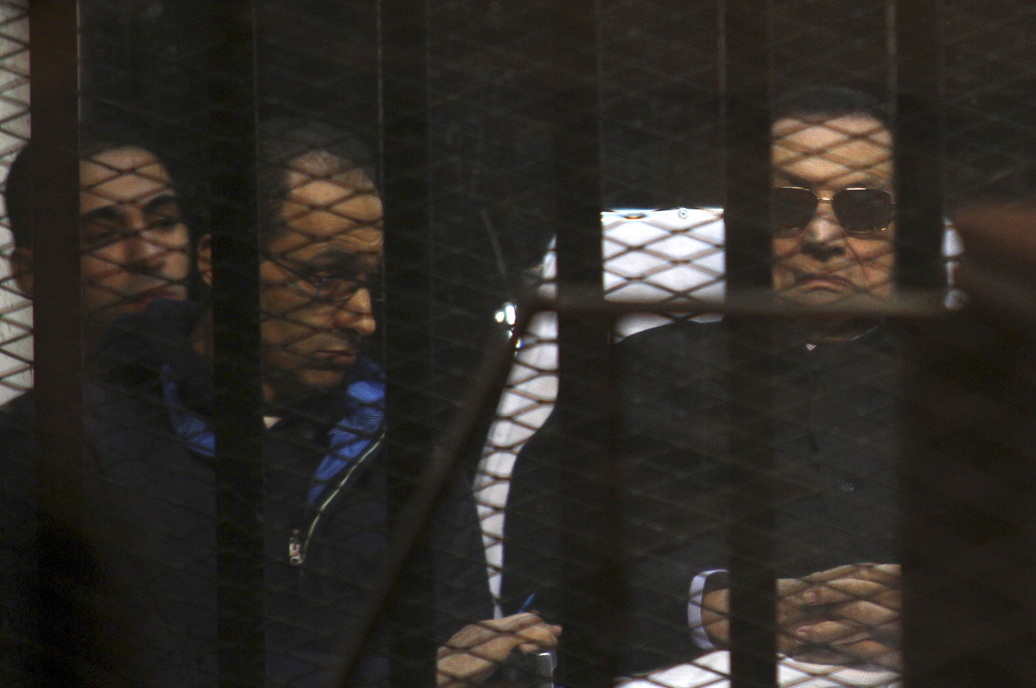 Ousted Egyptian President Hosni Mubarak, 86, lies on a gurney next to his son Gamal, second left, in the defendants cage during a court hearing in Cairo, Egypt