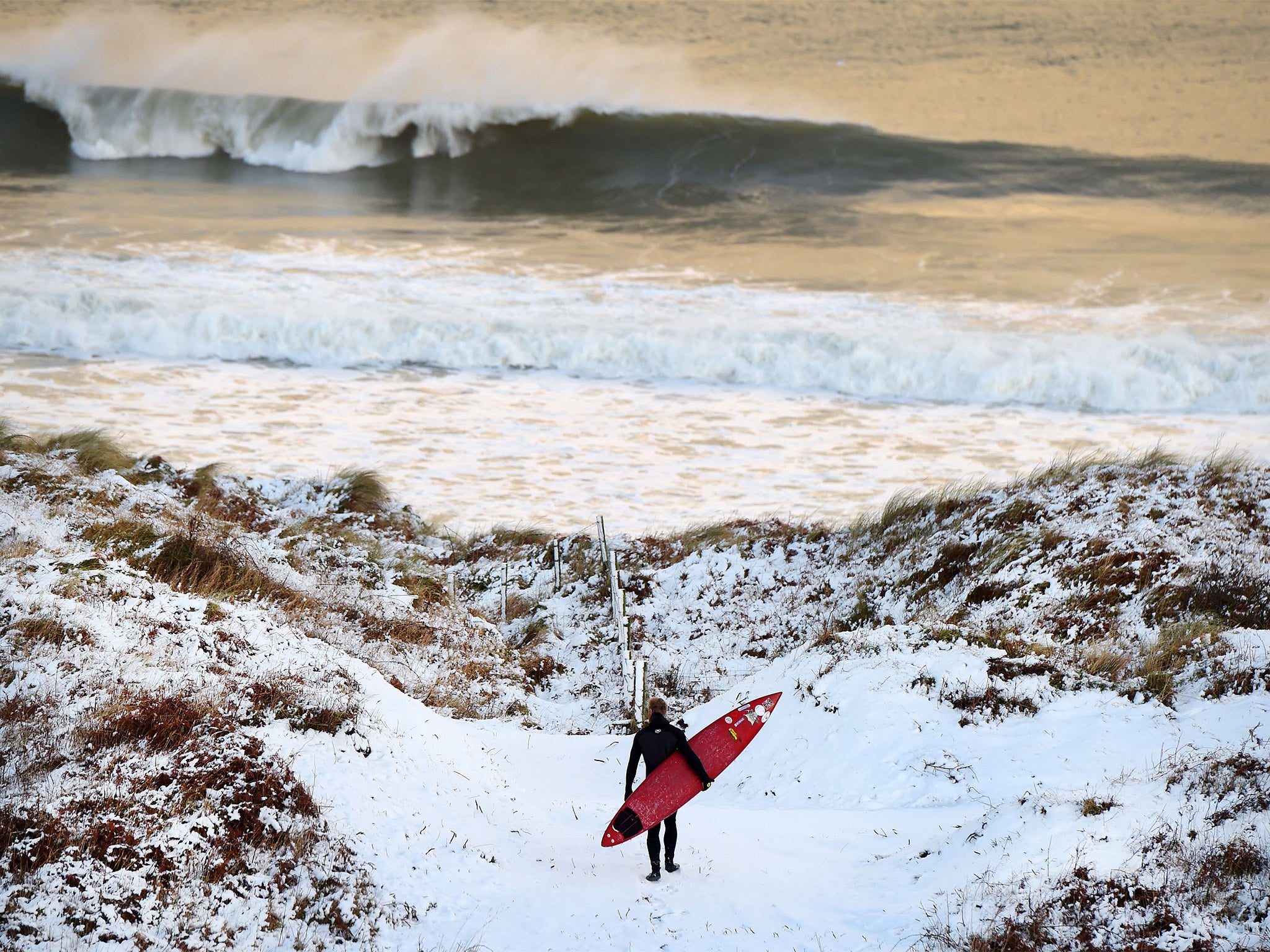 A surfer makes his way towards the beach at Portrush in Antrim, Northern Ireland, on Wednesday, where heavy snowfall led to traffic disruption and school closures