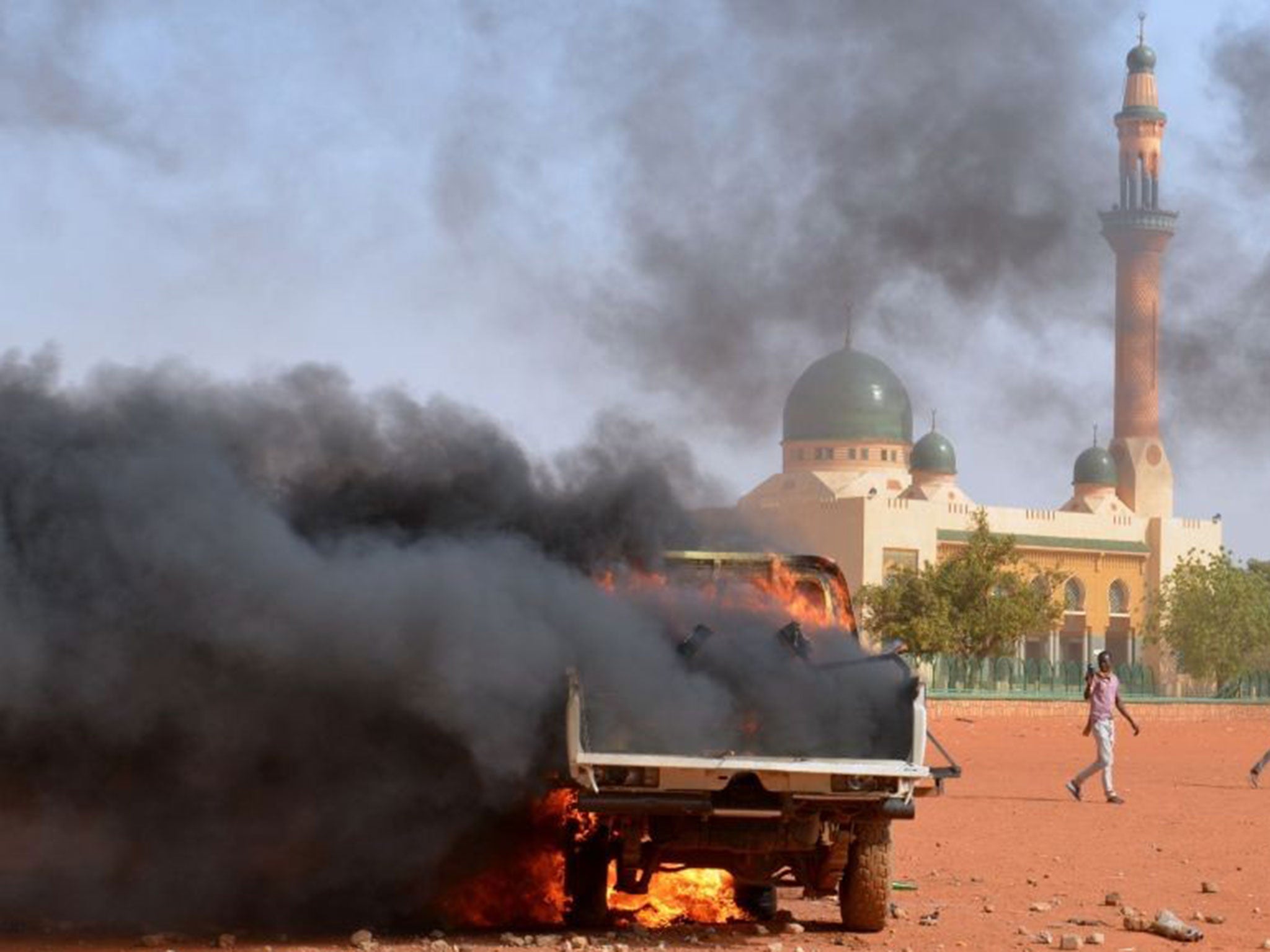 People run past a police truck on fire by protesters during a demonstration against French weekly Charlie Hebdo's publication of a cartoon of the Prophet Mohamed in front of the grand mosque in Niamey