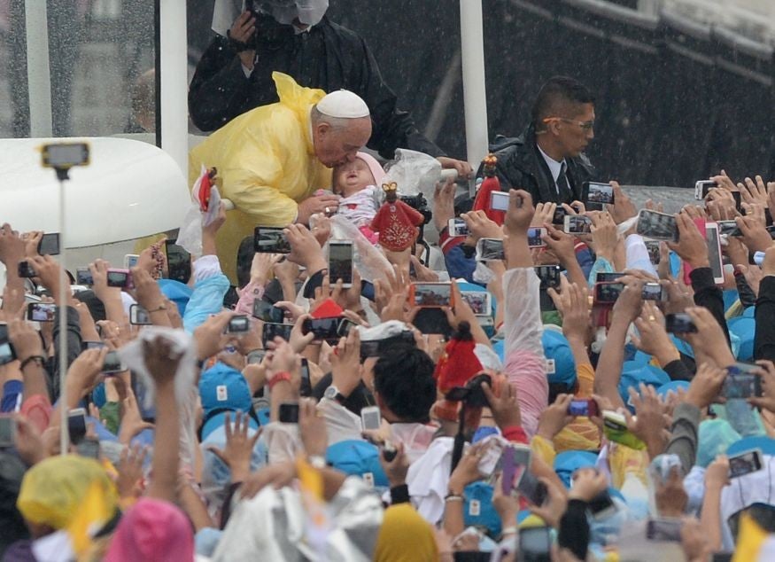 A sea of phones are held up while the Pope kisses a baby