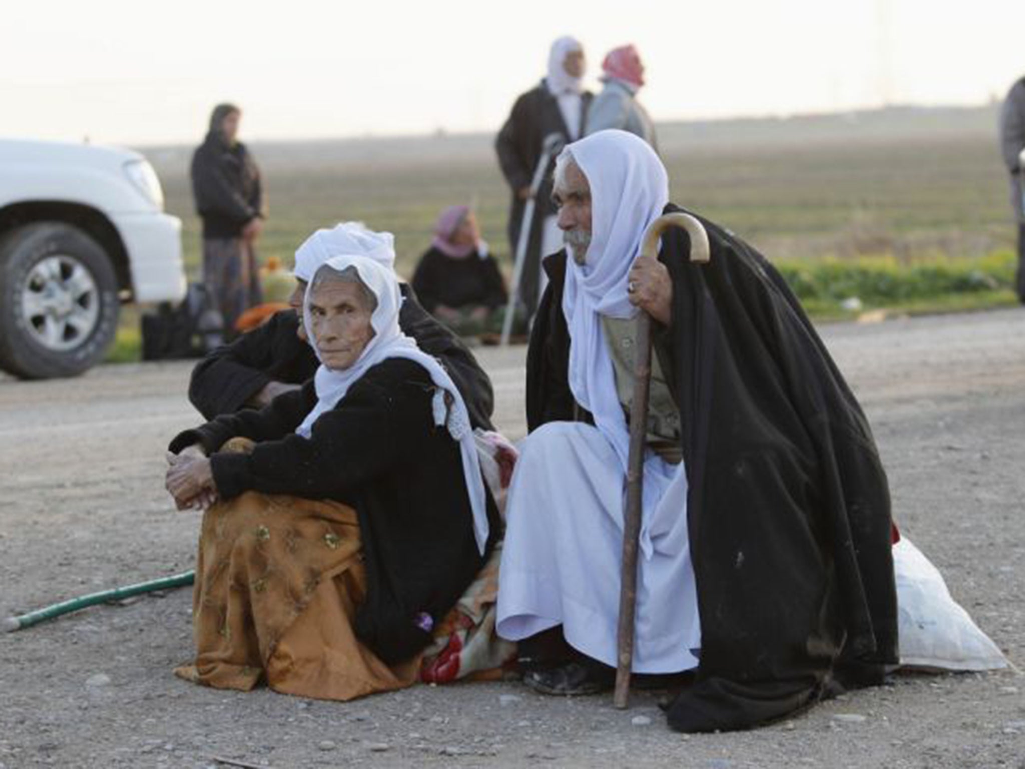 Elderly members of the Yazidi sect wait beside a road near Kirkuk after being released by their Isis captors on Saturday. They report continuing mistreatment of those still held captive (Reuters)