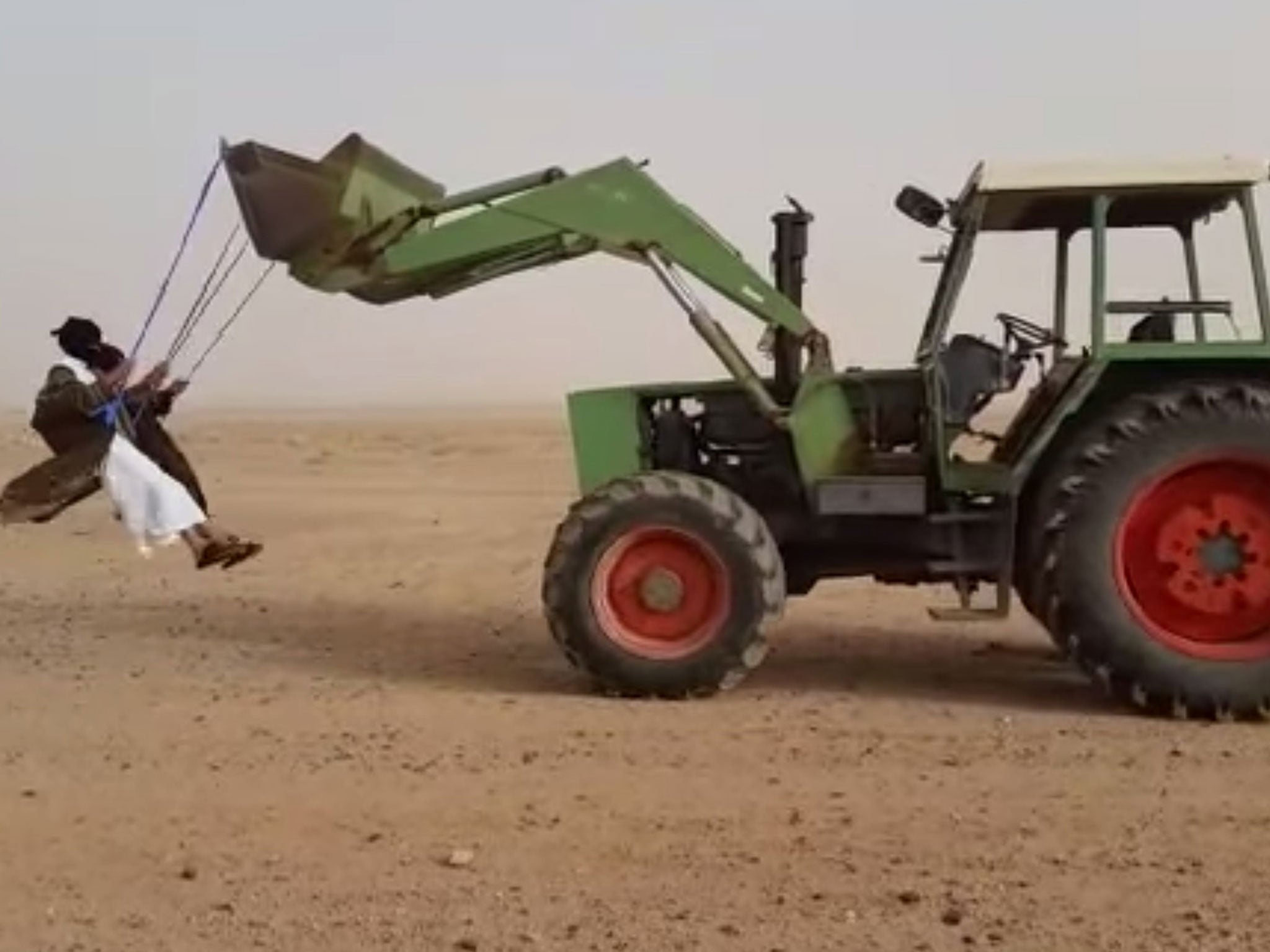 Men 'ghost swing' on a driverless tractor reversing slowly in the desert