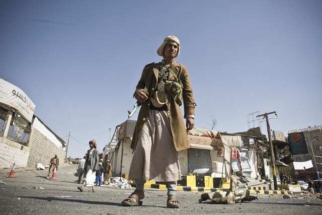 A Houthi Shiite Yemeni stands guard in front of a building damaged during recent clashes near the presidential palace in Sanaa