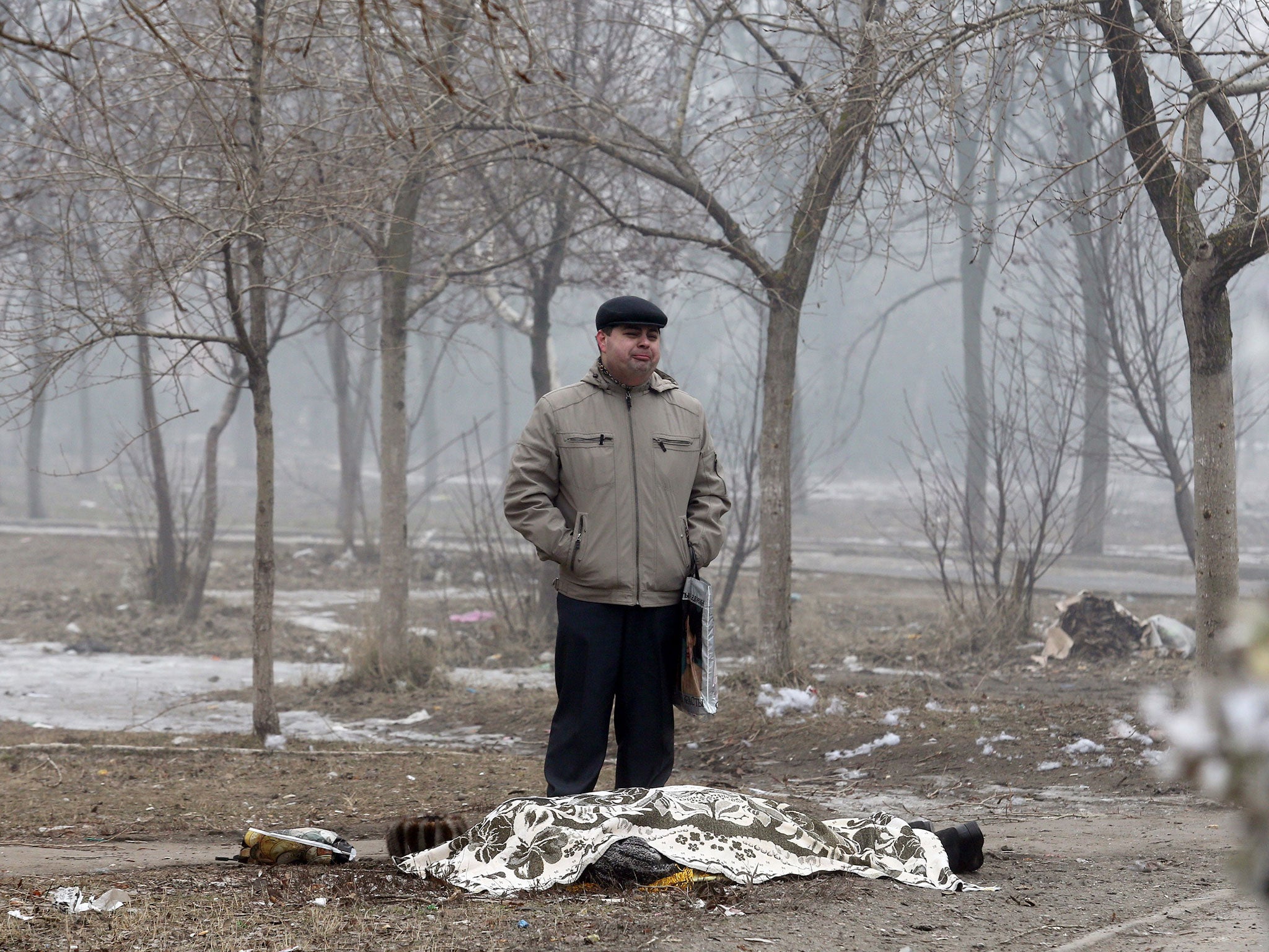 A man stands beside the covered body of a man who died after shelling in the southern Ukrainian port city of Mariupol