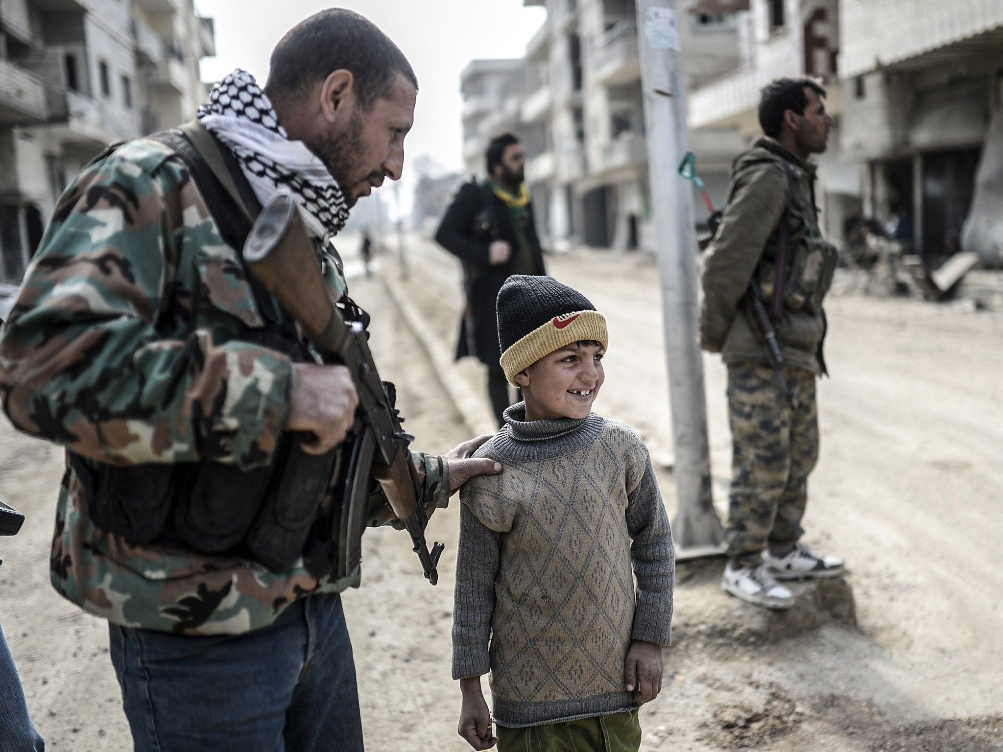 A Kurdish fighter walks with his child in Kobani after Kurdish forces recaptured the strategic Syrian border town (Getty)